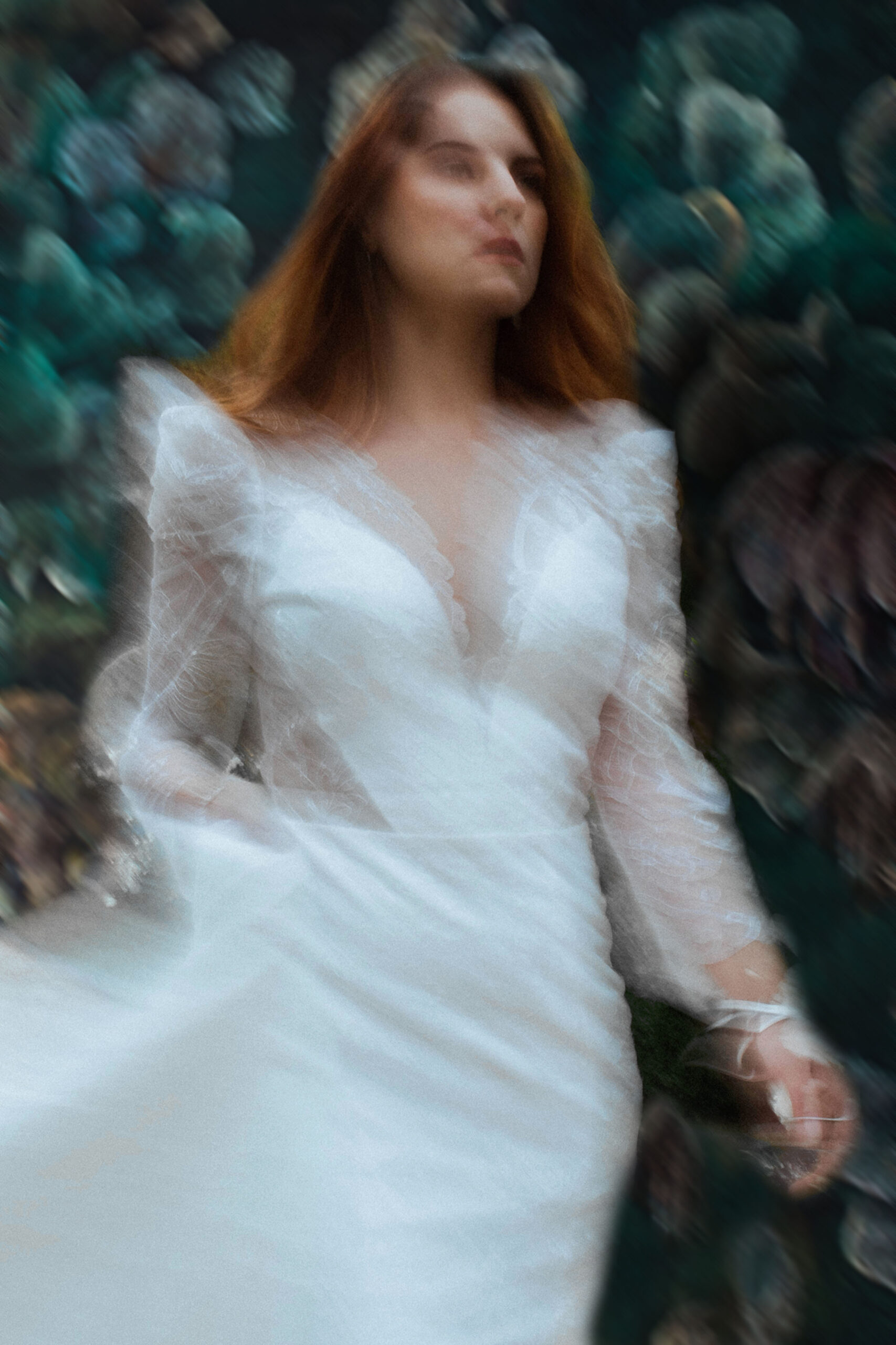 Femme portant une robe de mariée en dentelle devant un fond fleuri.