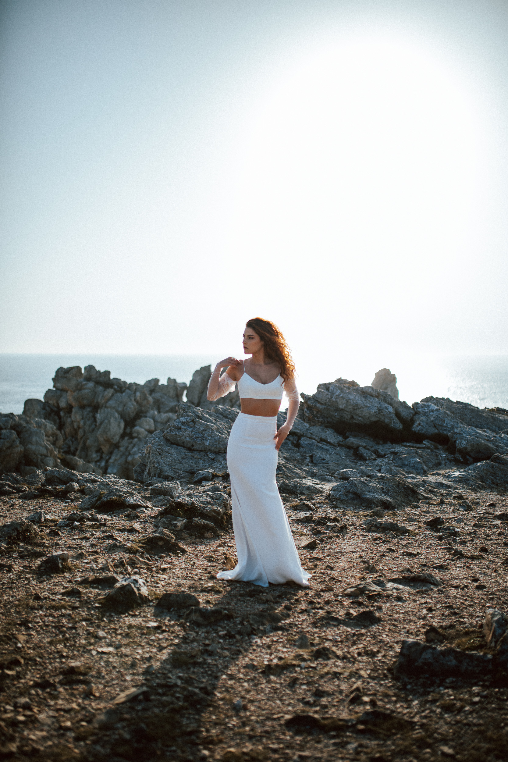 Femme rousse portant une robe de mariée brodée de perles en bord de mer.