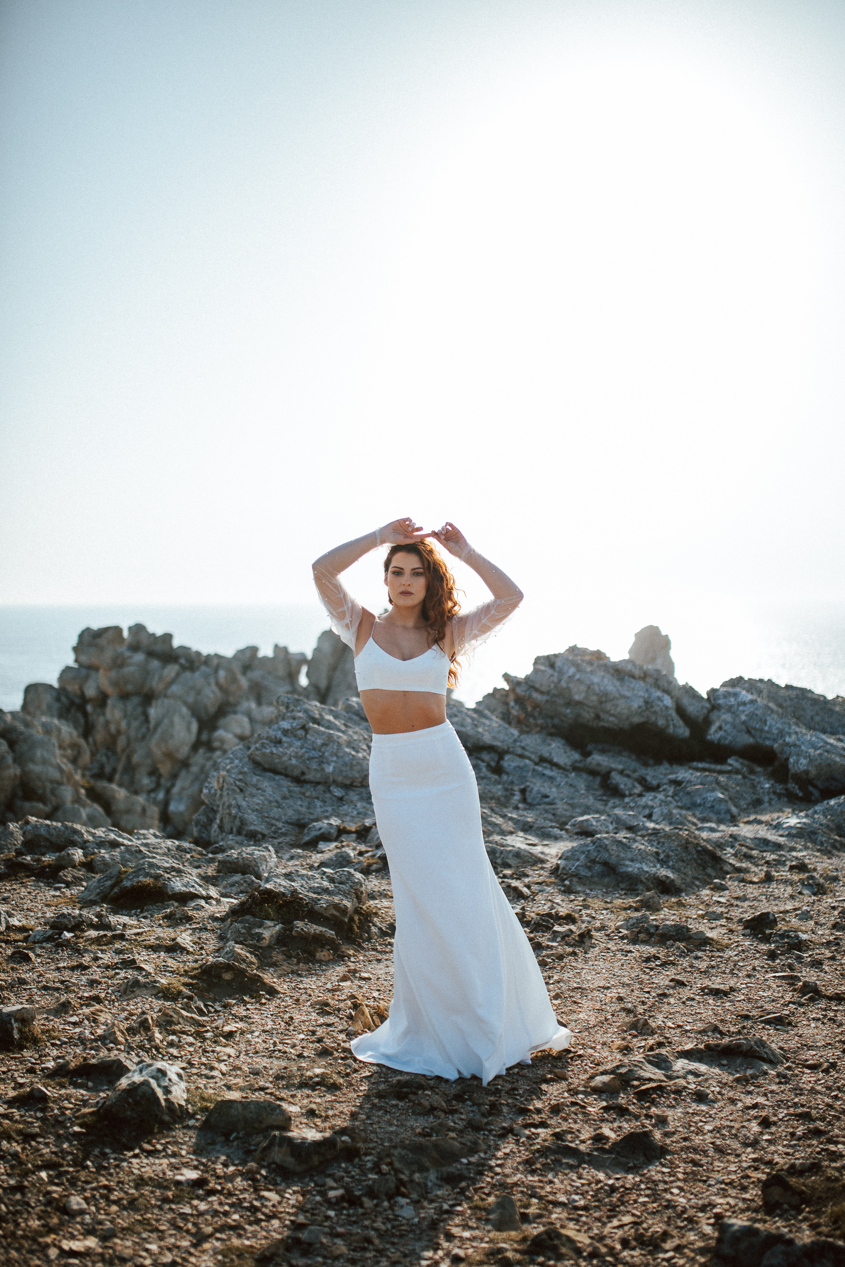 Femme rousse portant une robe de mariée brodée de perles en bord de mer.