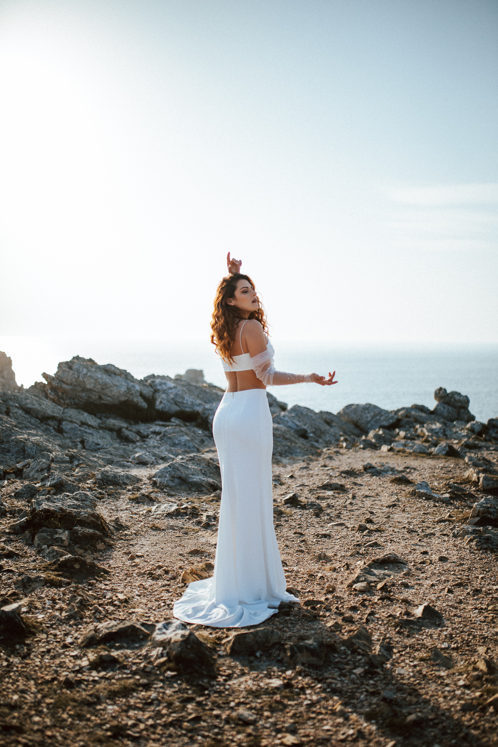Femme rousse portant une robe de mariée brodée de perles en bord de mer.