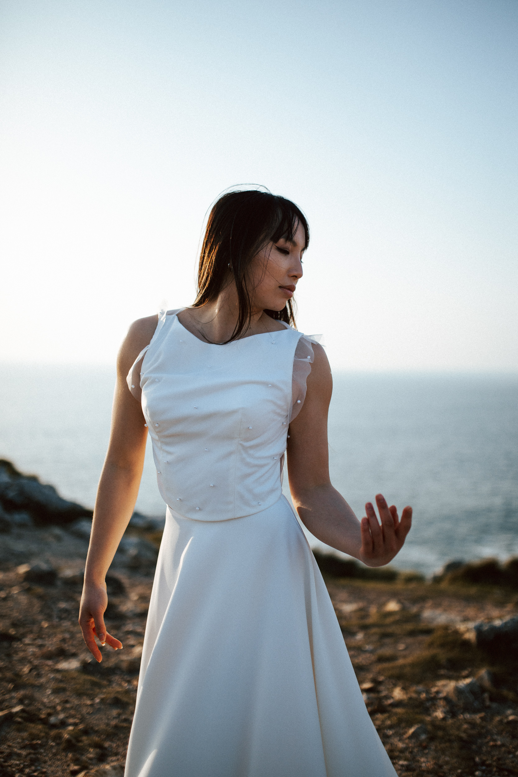 Femme asiatique portant une robe de mariée brodée de perles en bord de mer.