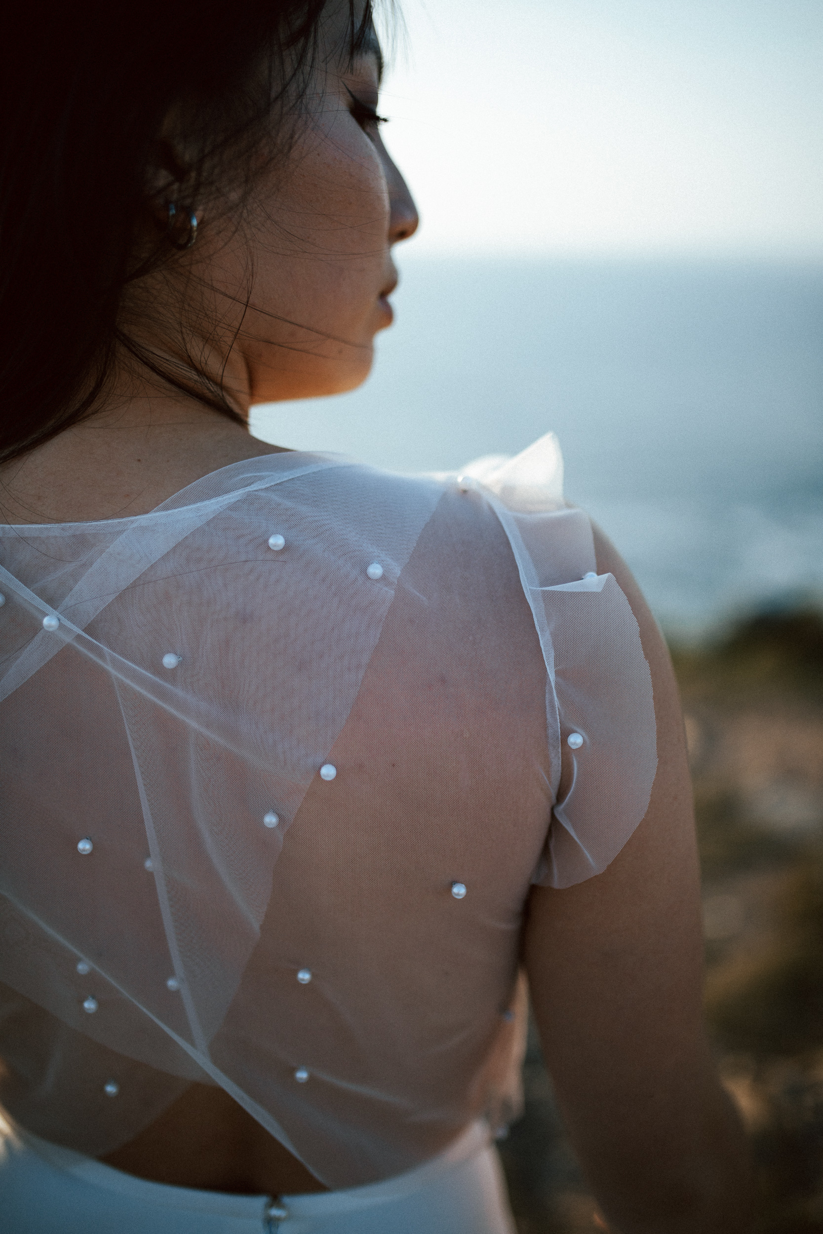 Femme asiatique portant une robe de mariée brodée de perles en bord de mer.