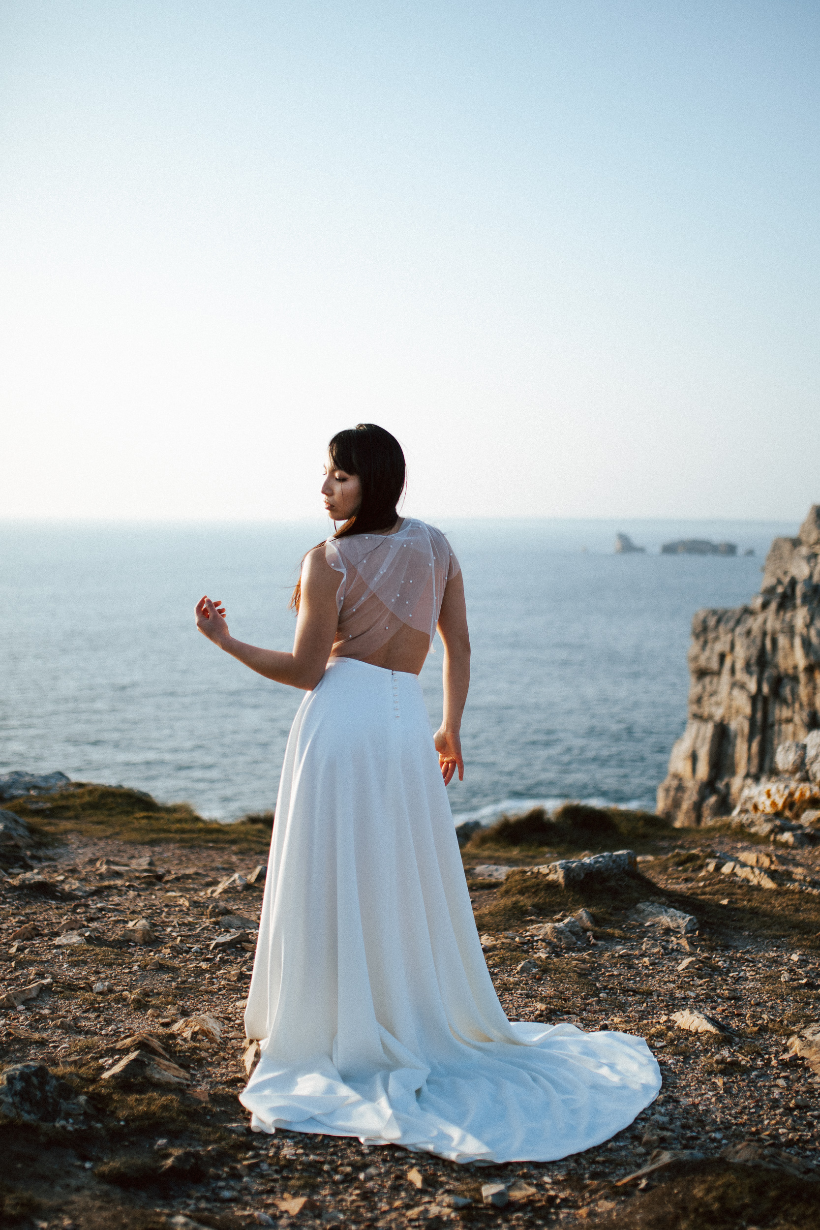 Femme asiatique portant une robe de mariée brodée de perles en bord de mer.
