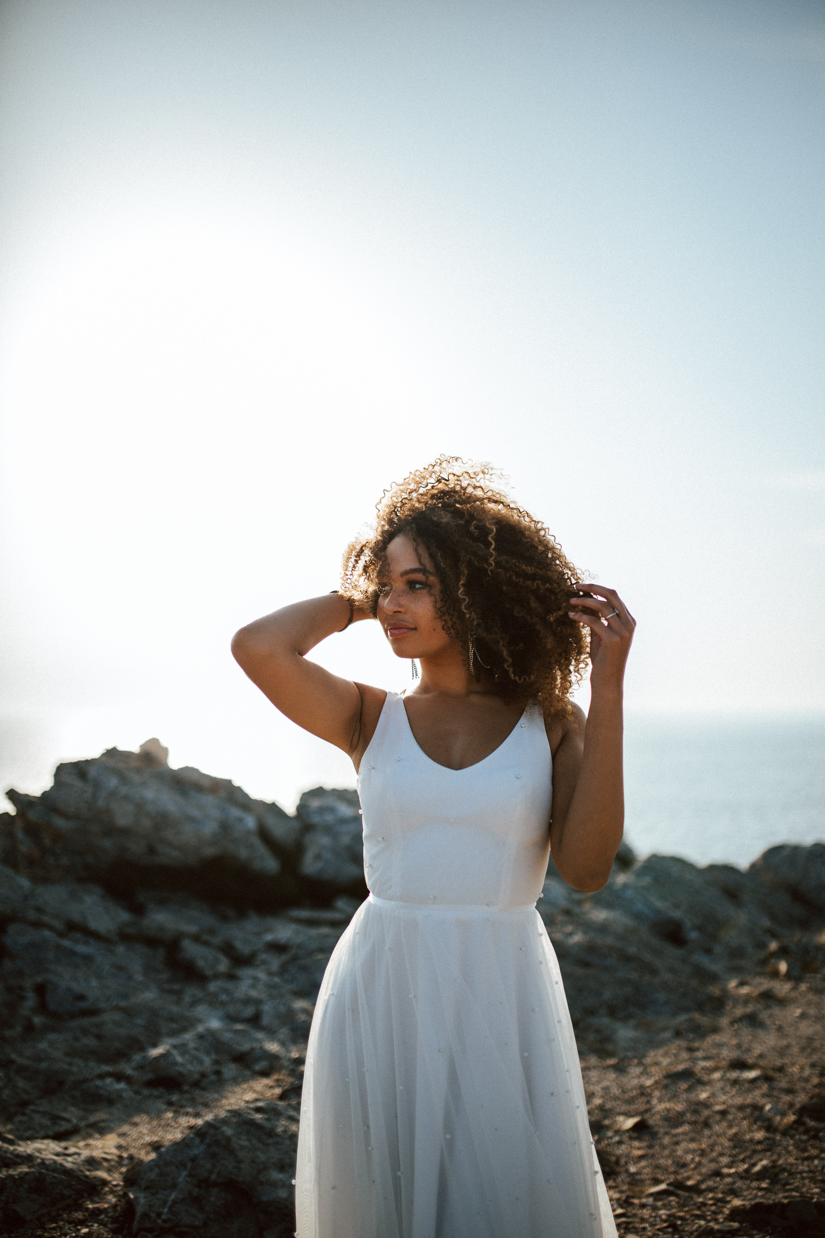 Femme métissée portant une robe de mariée brodée de perles en bord de mer.