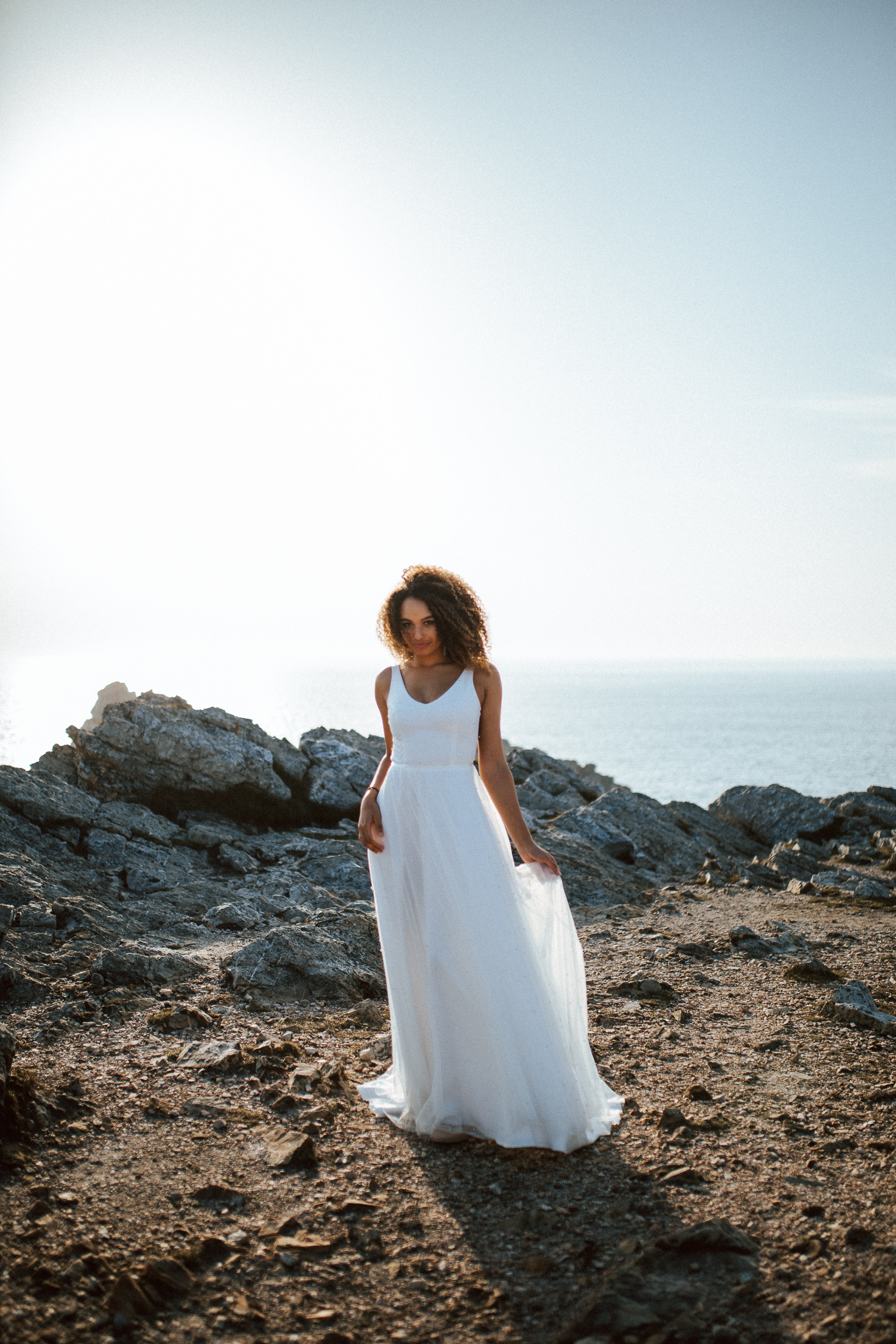 Femme métissée portant une robe de mariée brodée de perles en bord de mer.