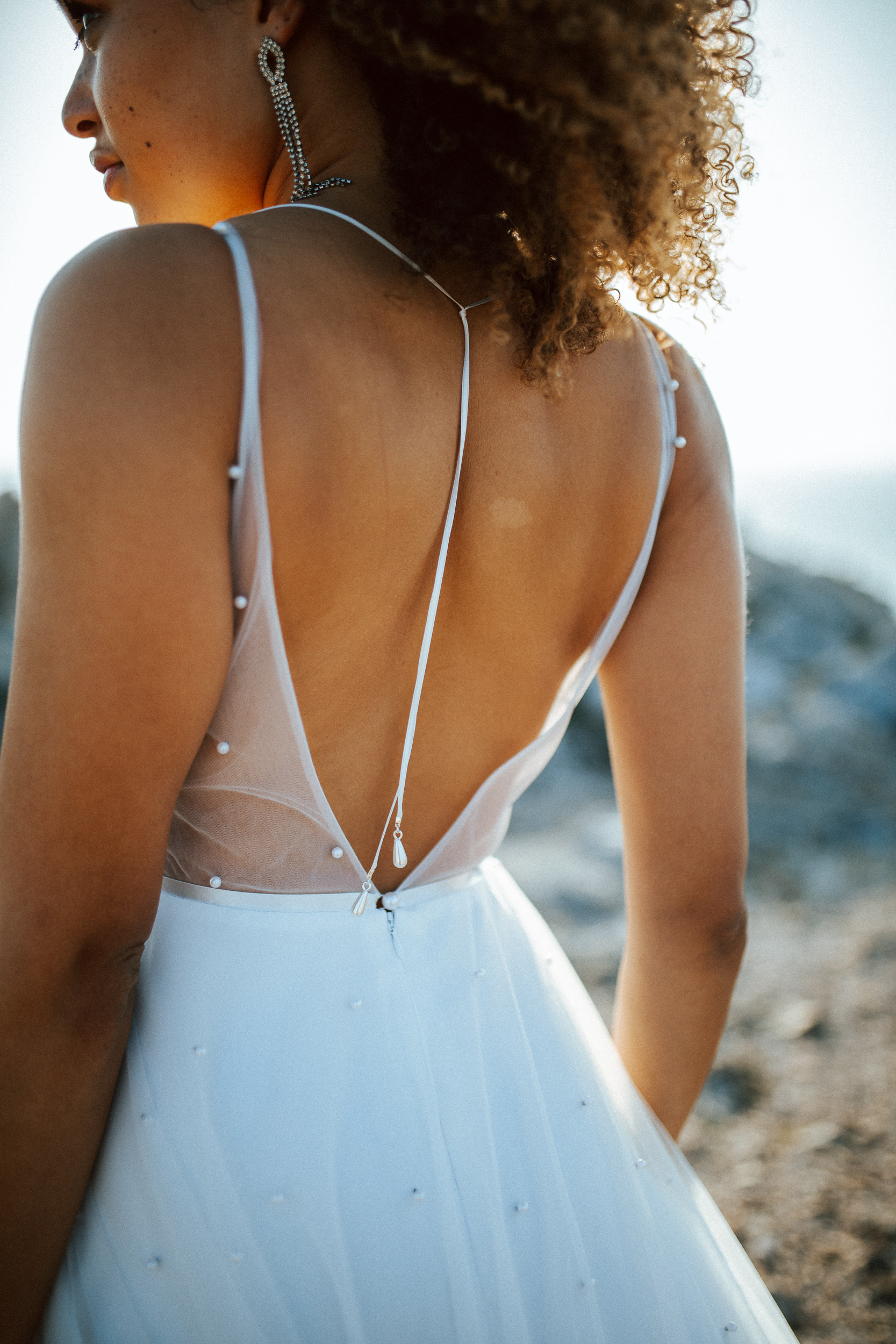 Femme métissée portant une robe de mariée brodée de perles en bord de mer.