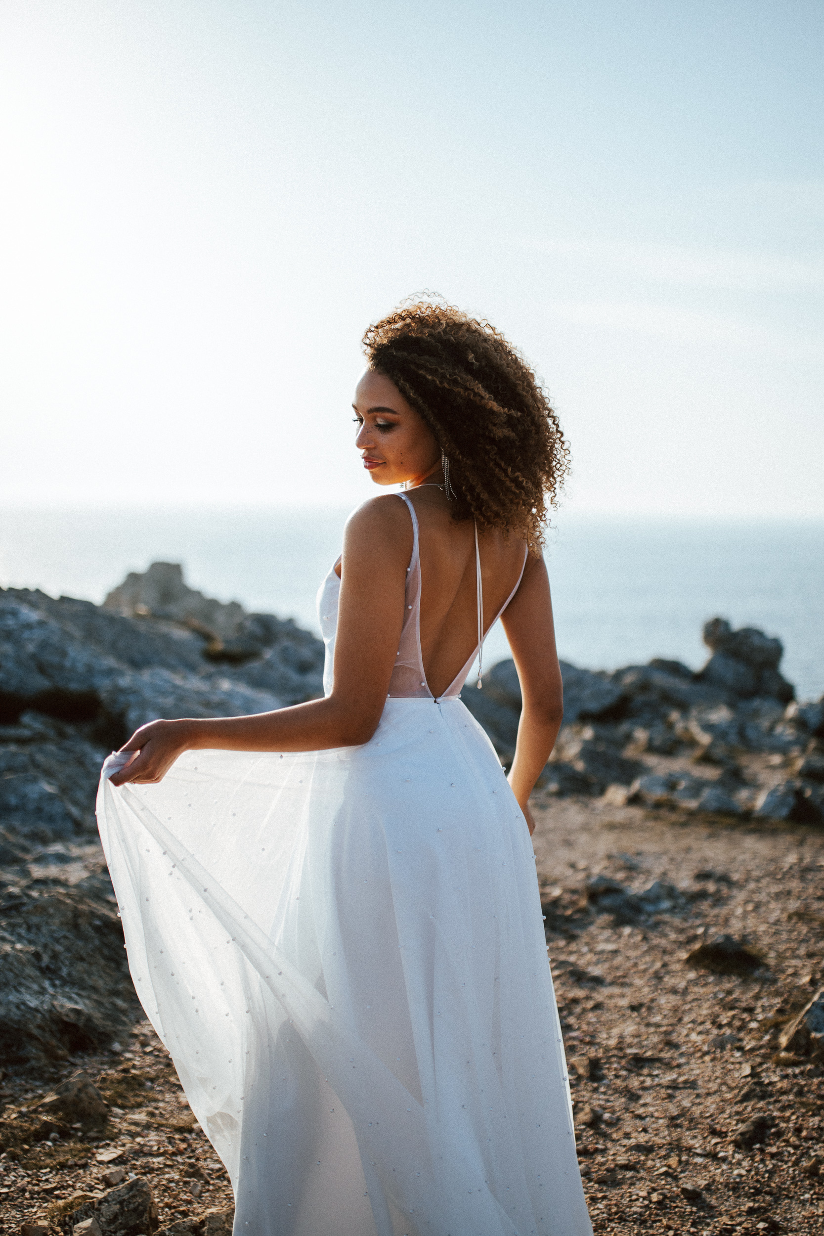 Femme métissée portant une robe de mariée brodée de perles en bord de mer.