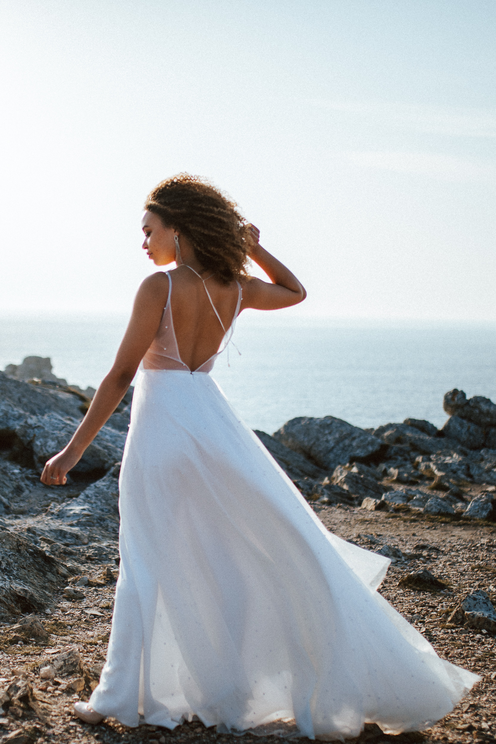 Femme métissée portant une robe de mariée brodée de perles en bord de mer.