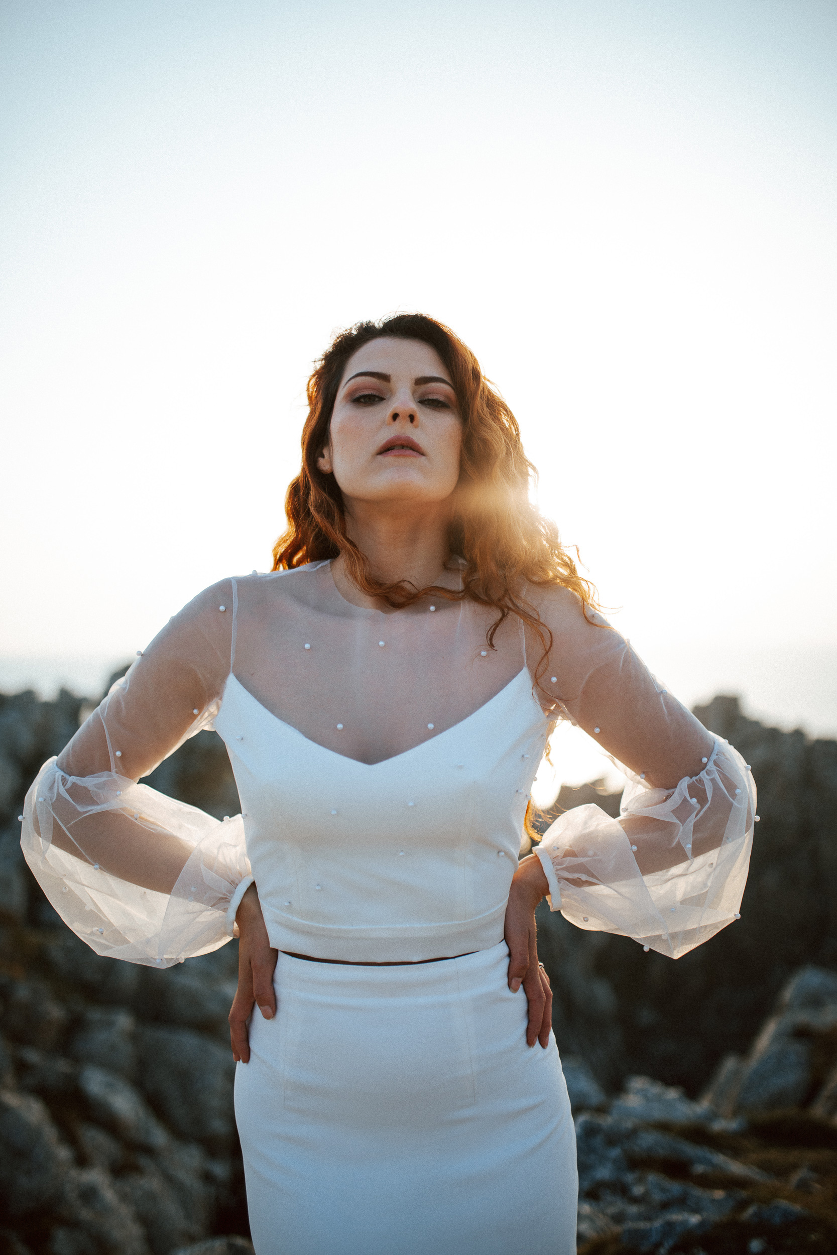 Femme rousse portant une robe de mariée brodée de perles en bord de mer.