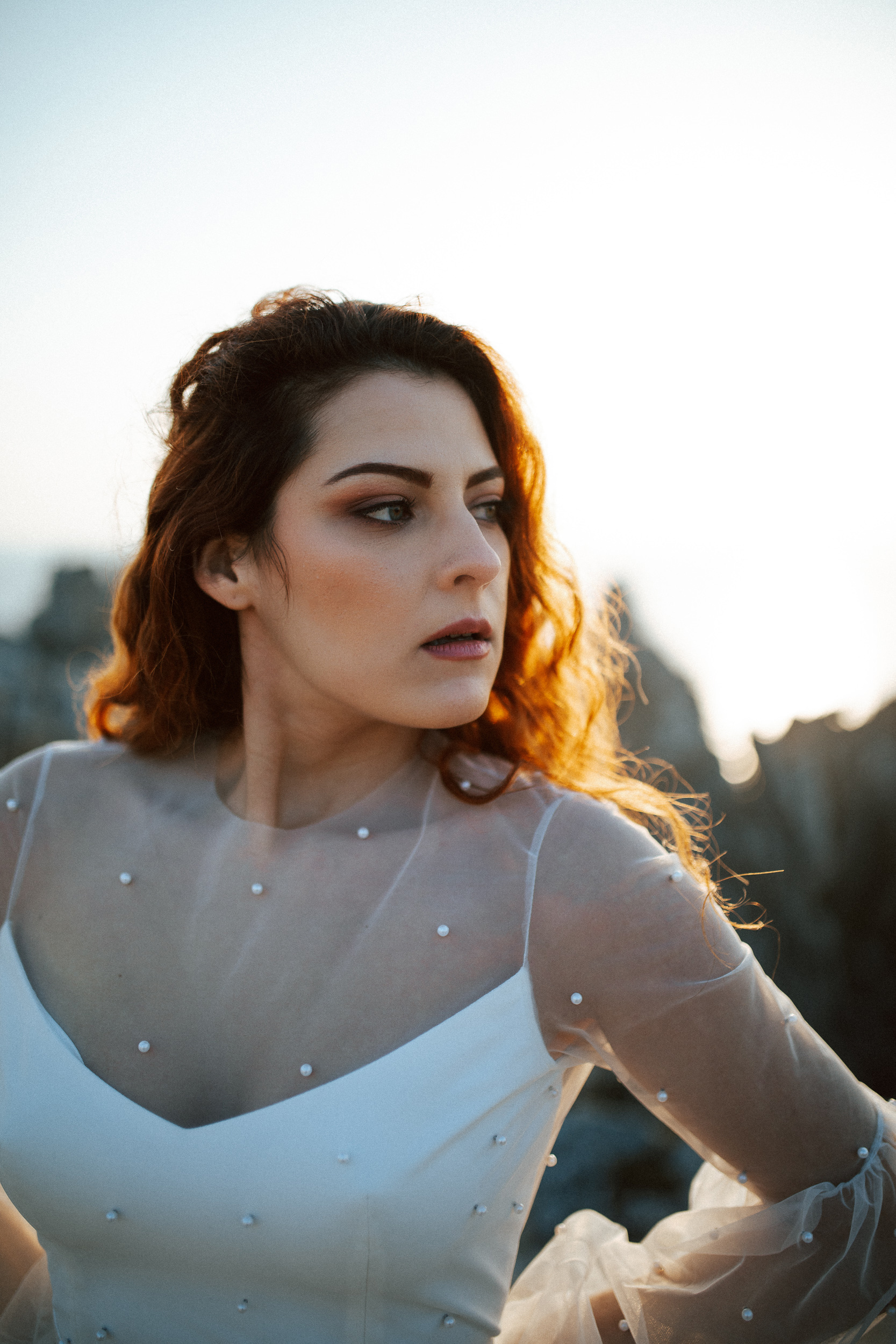 Femme rousse portant une robe de mariée brodée de perles en bord de mer.