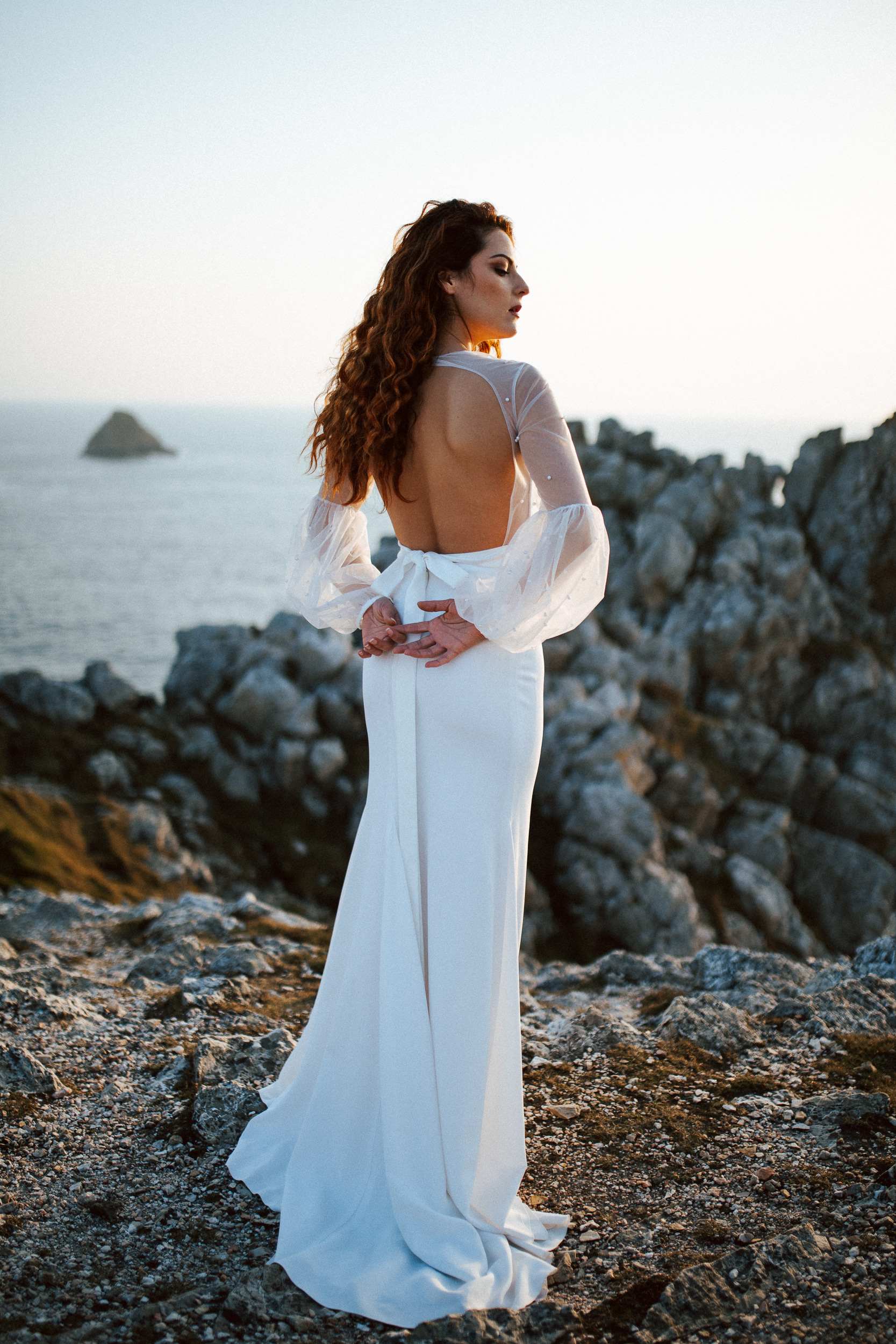 Femme rousse portant une robe de mariée brodée de perles en bord de mer.