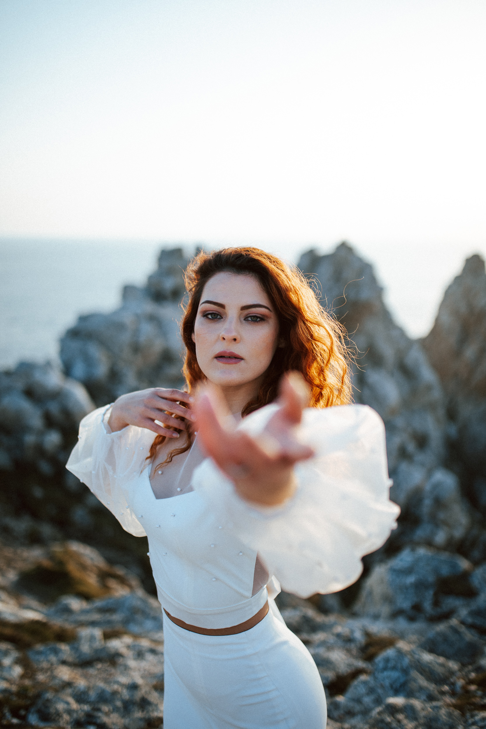 Femme rousse portant une robe de mariée brodée de perles en bord de mer.