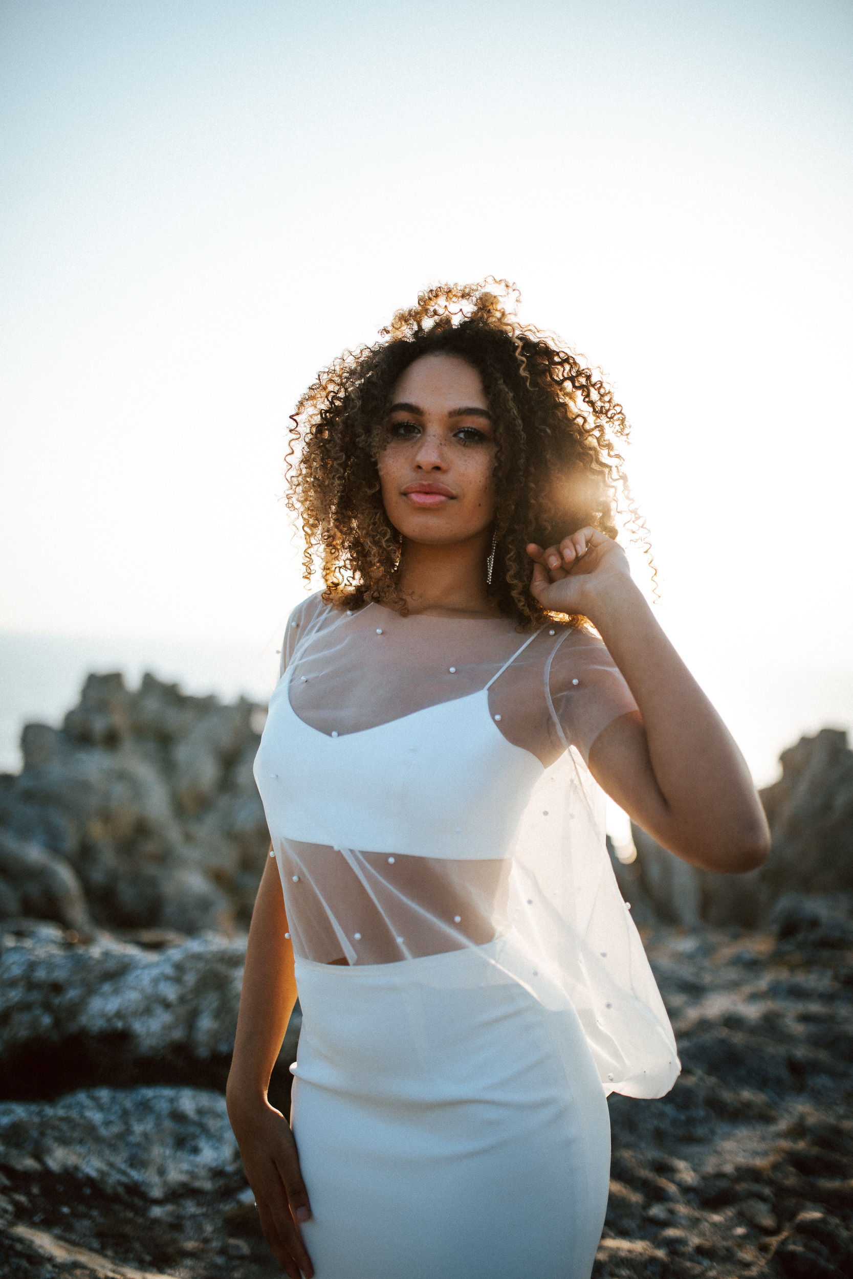 Femme métissée portant une robe de mariée brodée de perles en bord de mer.