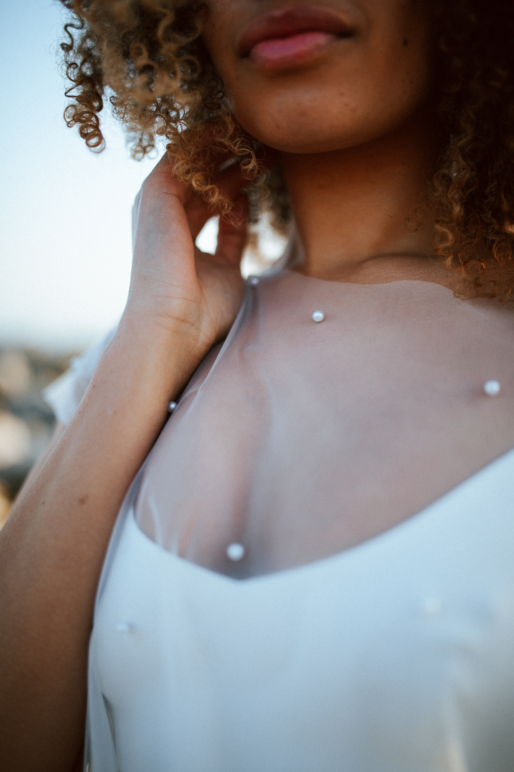 Femme métissée portant une robe de mariée brodée de perles en bord de mer.