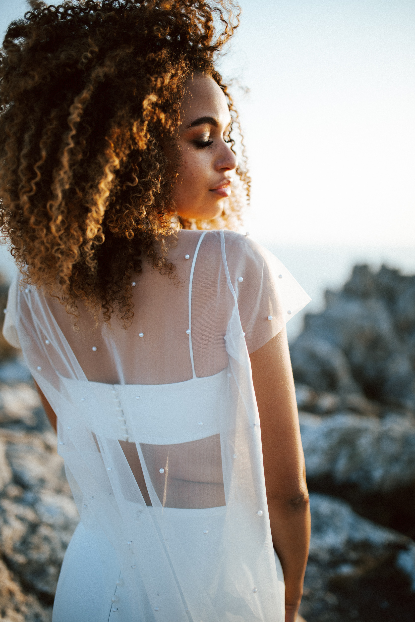 Femme métissée portant une robe de mariée brodée de perles en bord de mer.