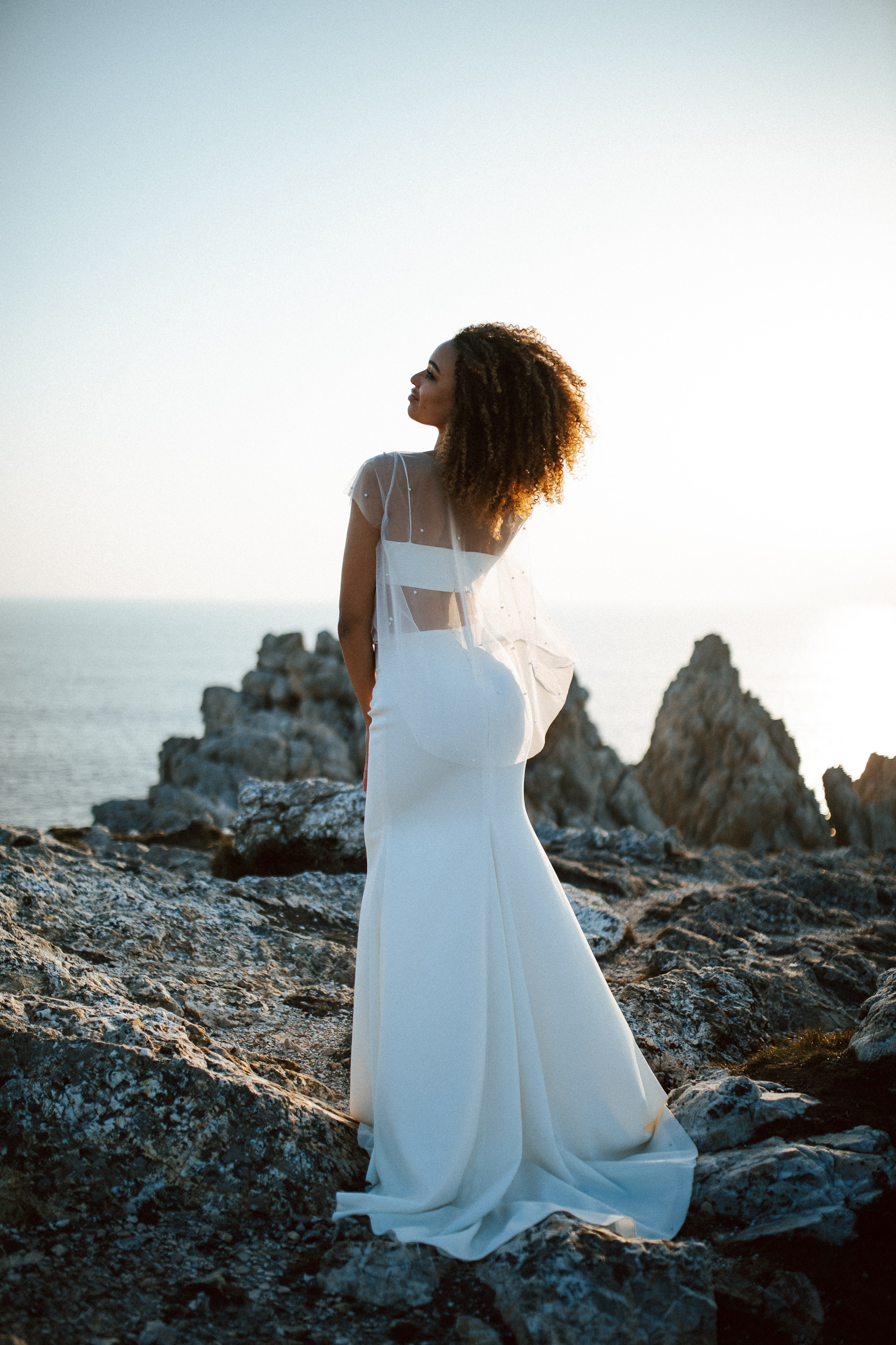 Femme métissée portant une robe de mariée brodée de perles en bord de mer.