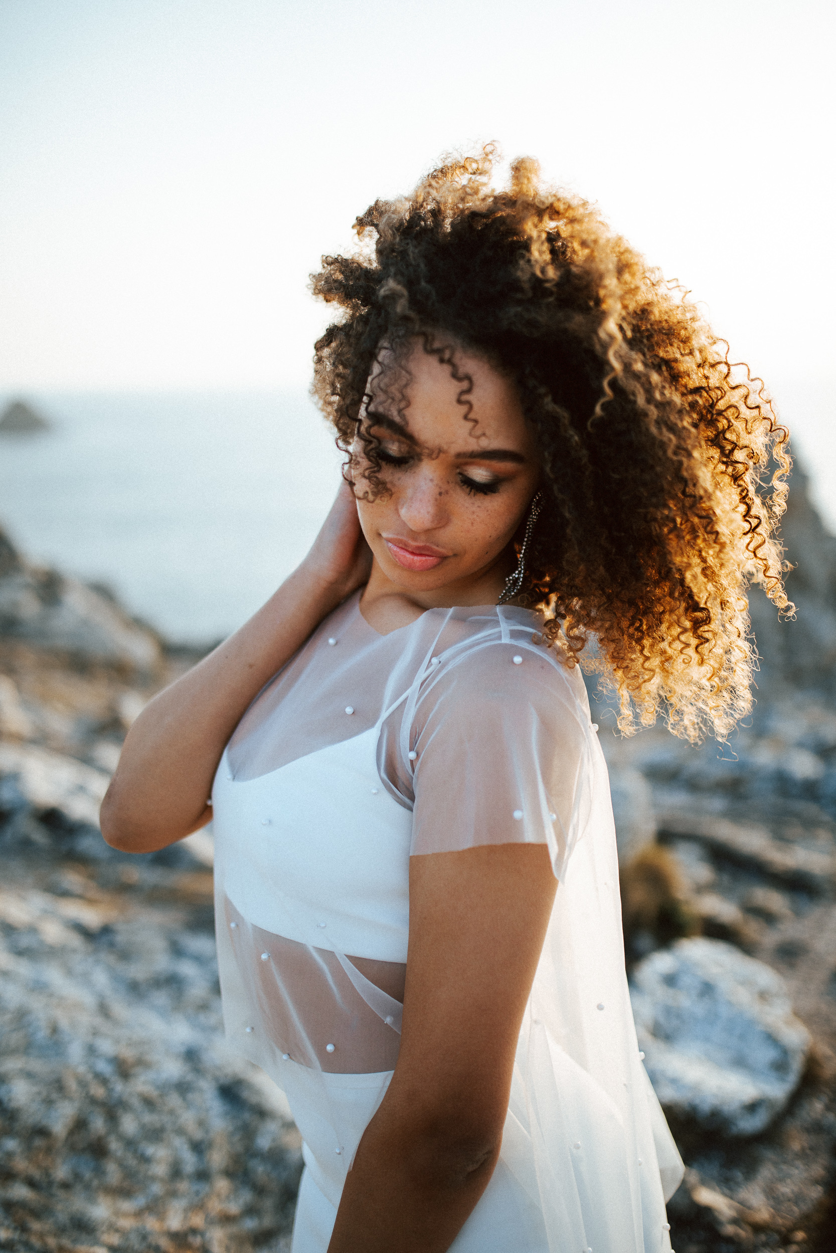 Femme métissée portant une robe de mariée brodée de perles en bord de mer.