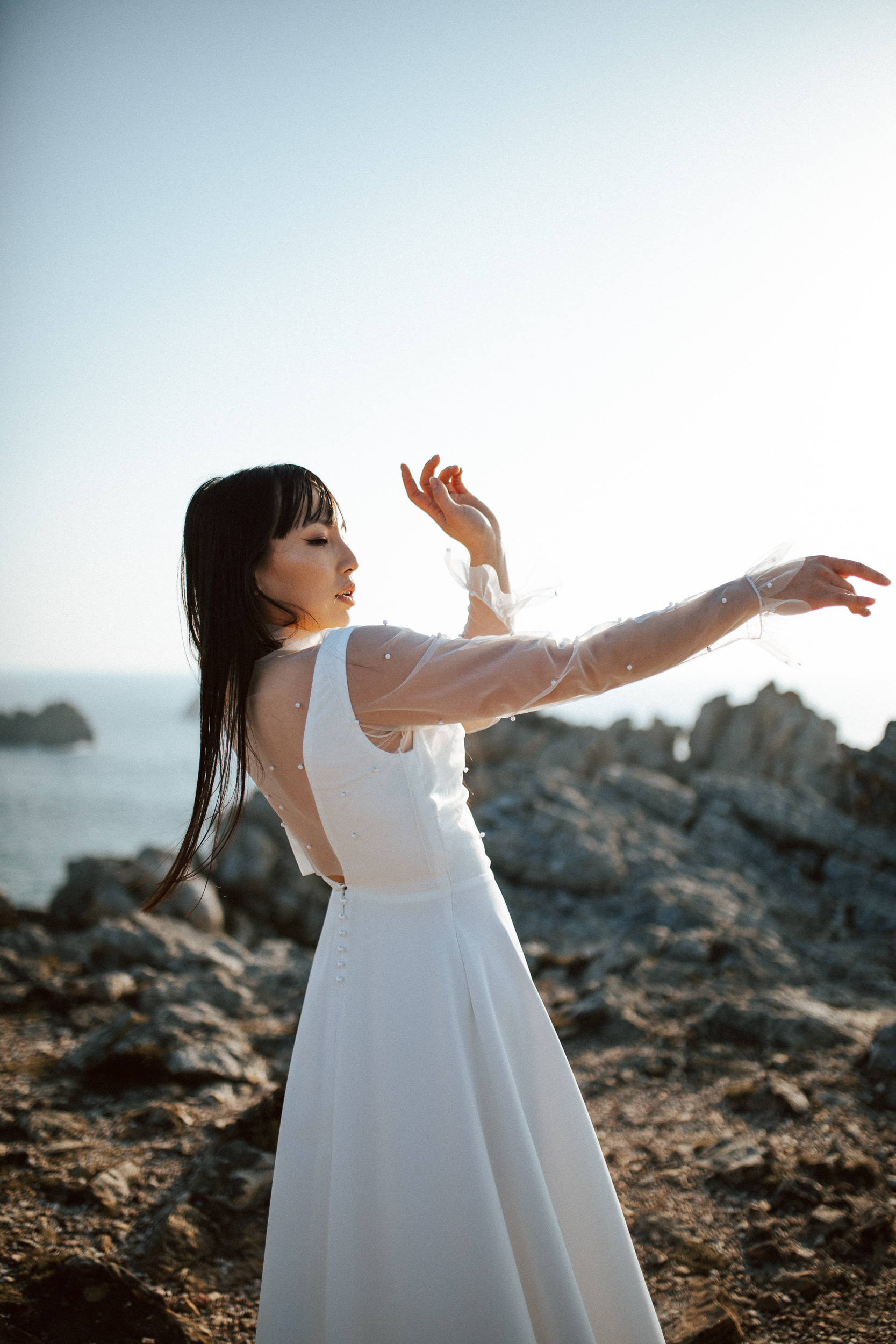 Femme asiatique portant une robe de mariée brodée de perles en bord de mer.