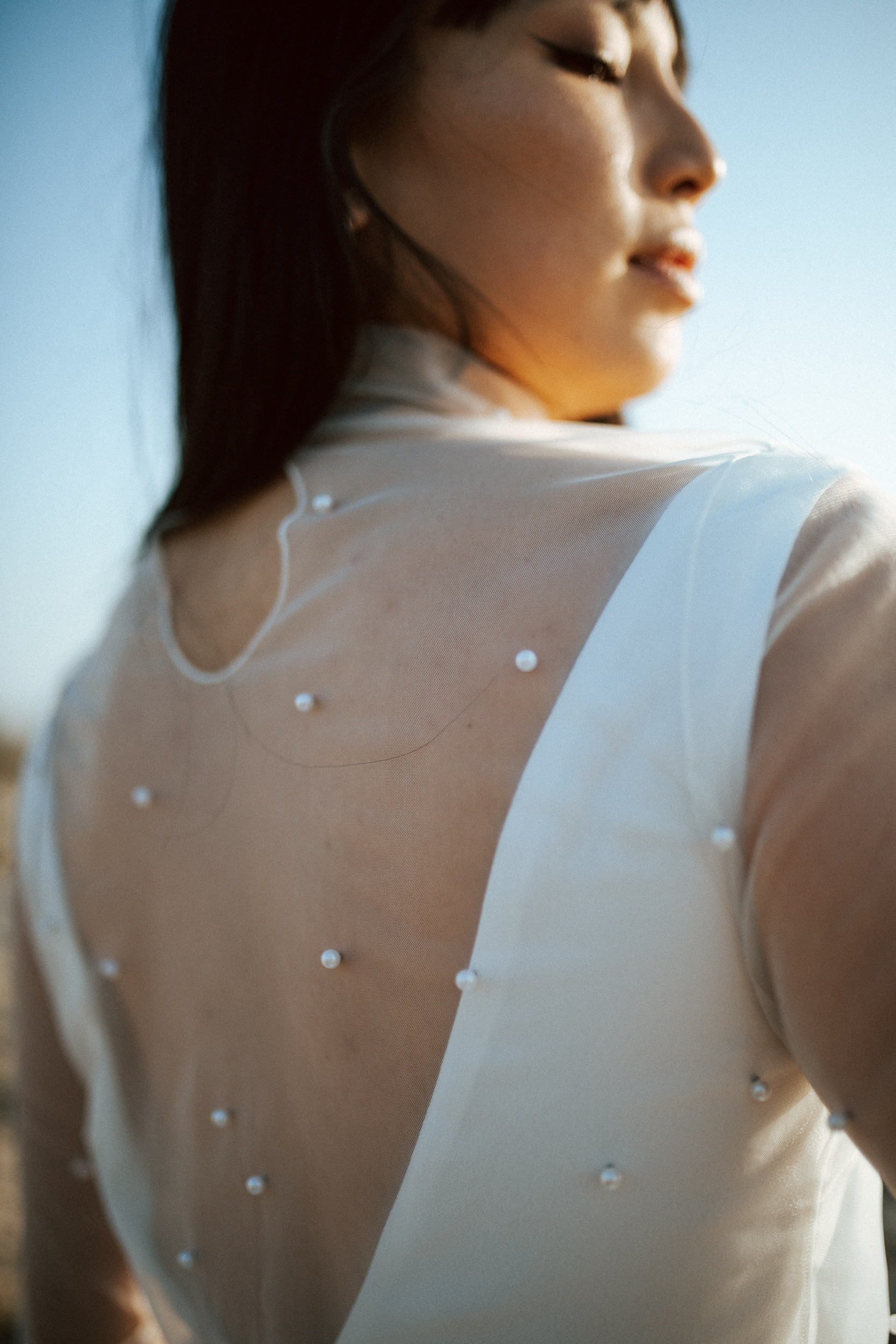 Femme asiatique portant une robe de mariée brodée de perles en bord de mer.