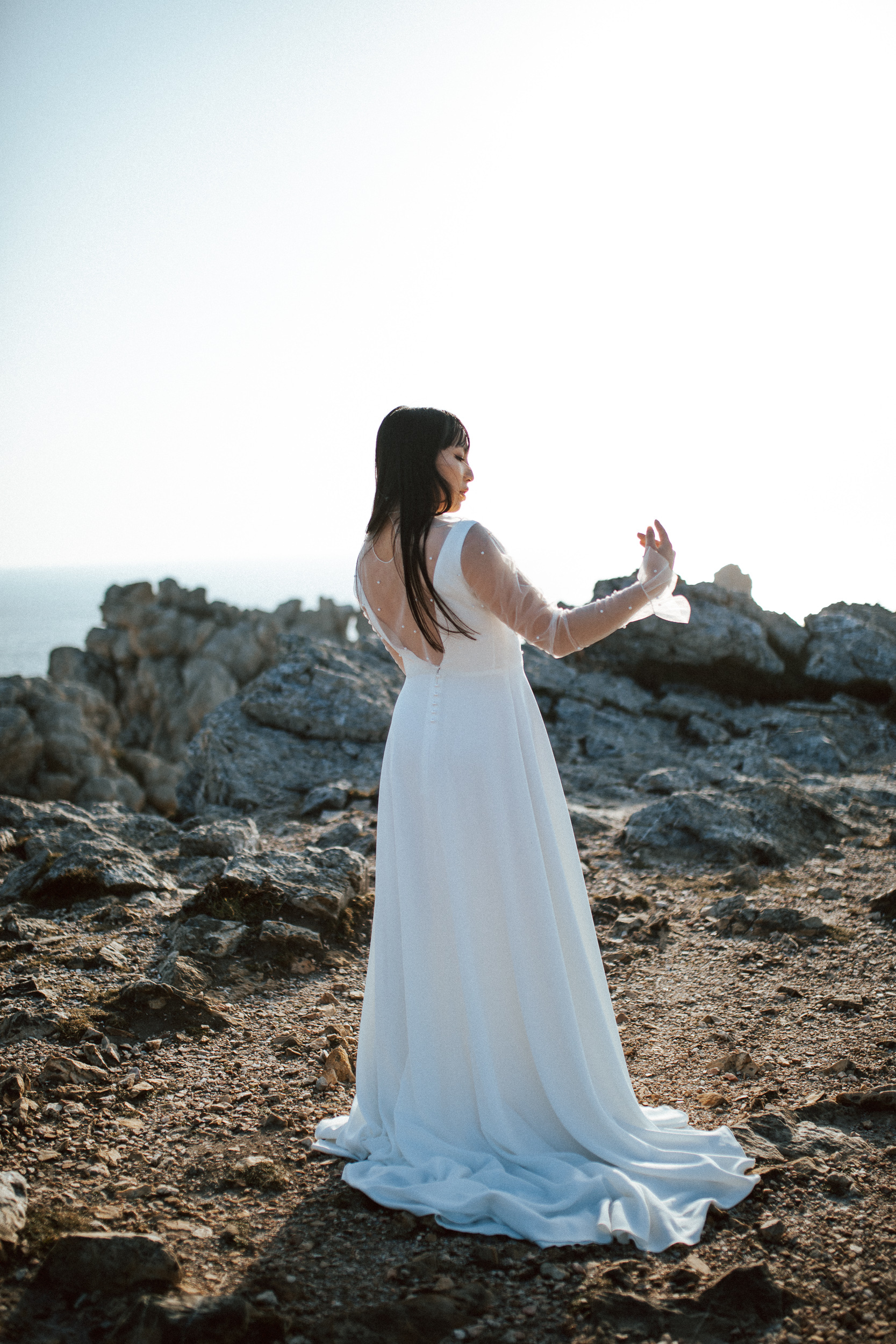 Femme asiatique portant une robe de mariée brodée de perles en bord de mer.