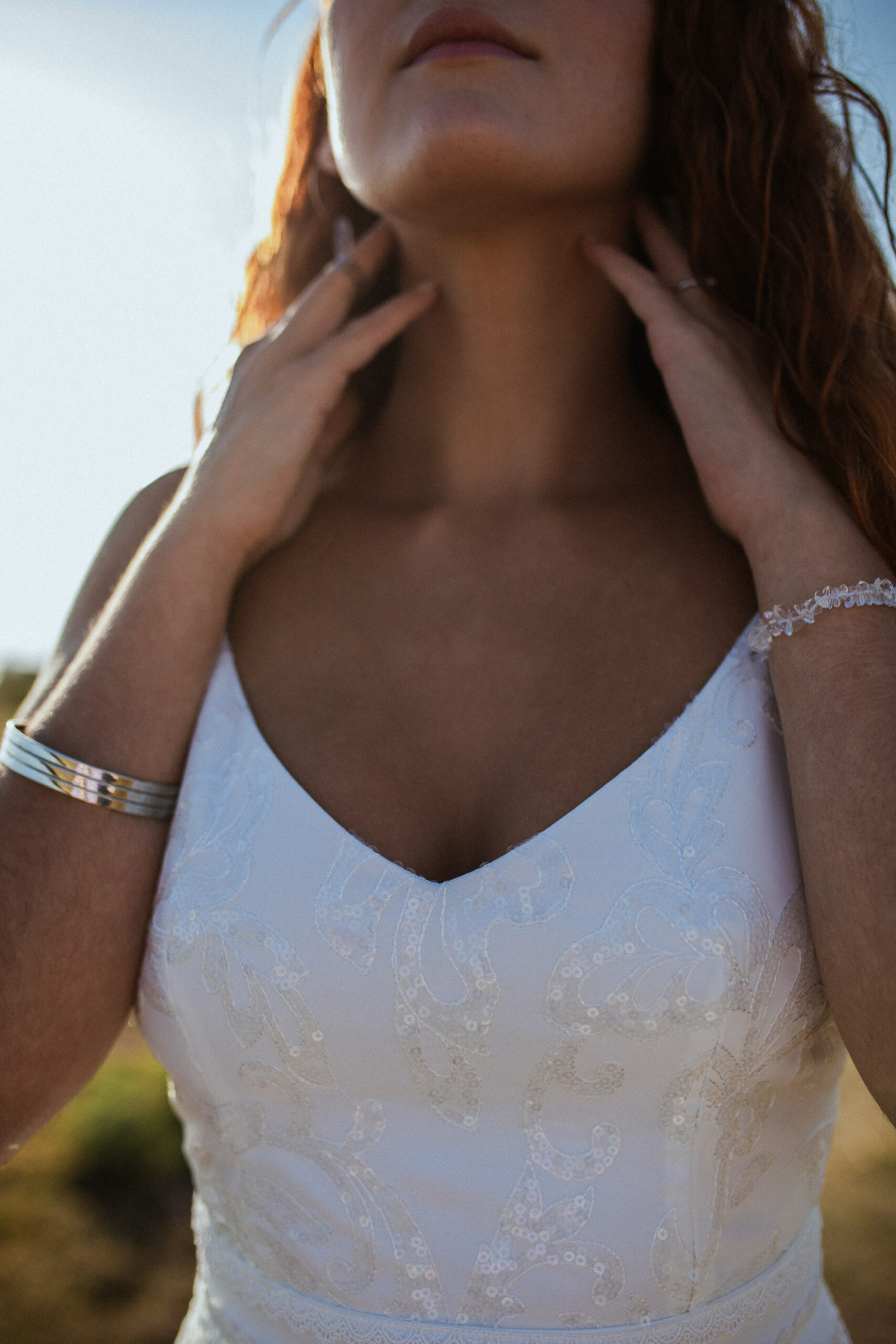 Femme rousse portant une robe de mariée en dentelle dans les dunes végétales en bord de mer.