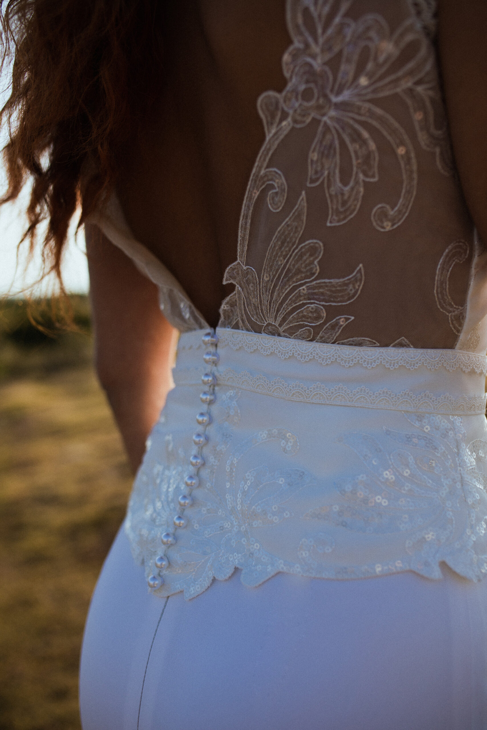 Femme rousse portant une robe de mariée en dentelle dans les dunes végétales en bord de mer.