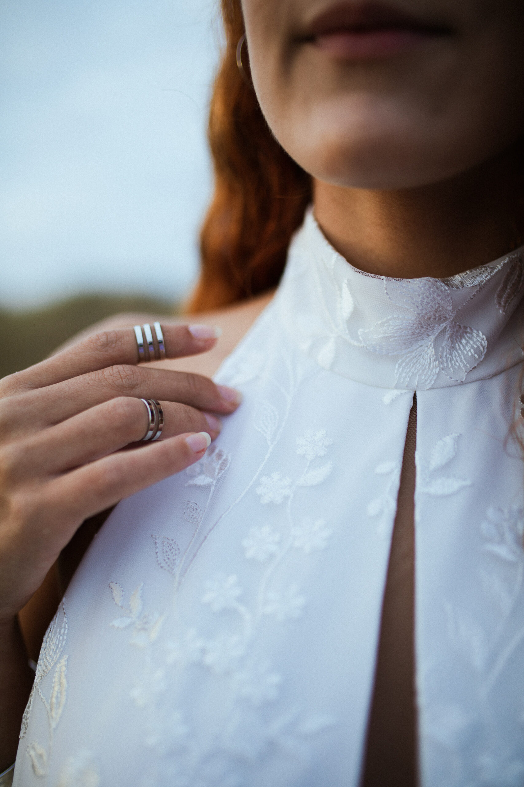 Femme rousse portant une robe de mariée en dentelle dans les dunes végétales en bord de mer.