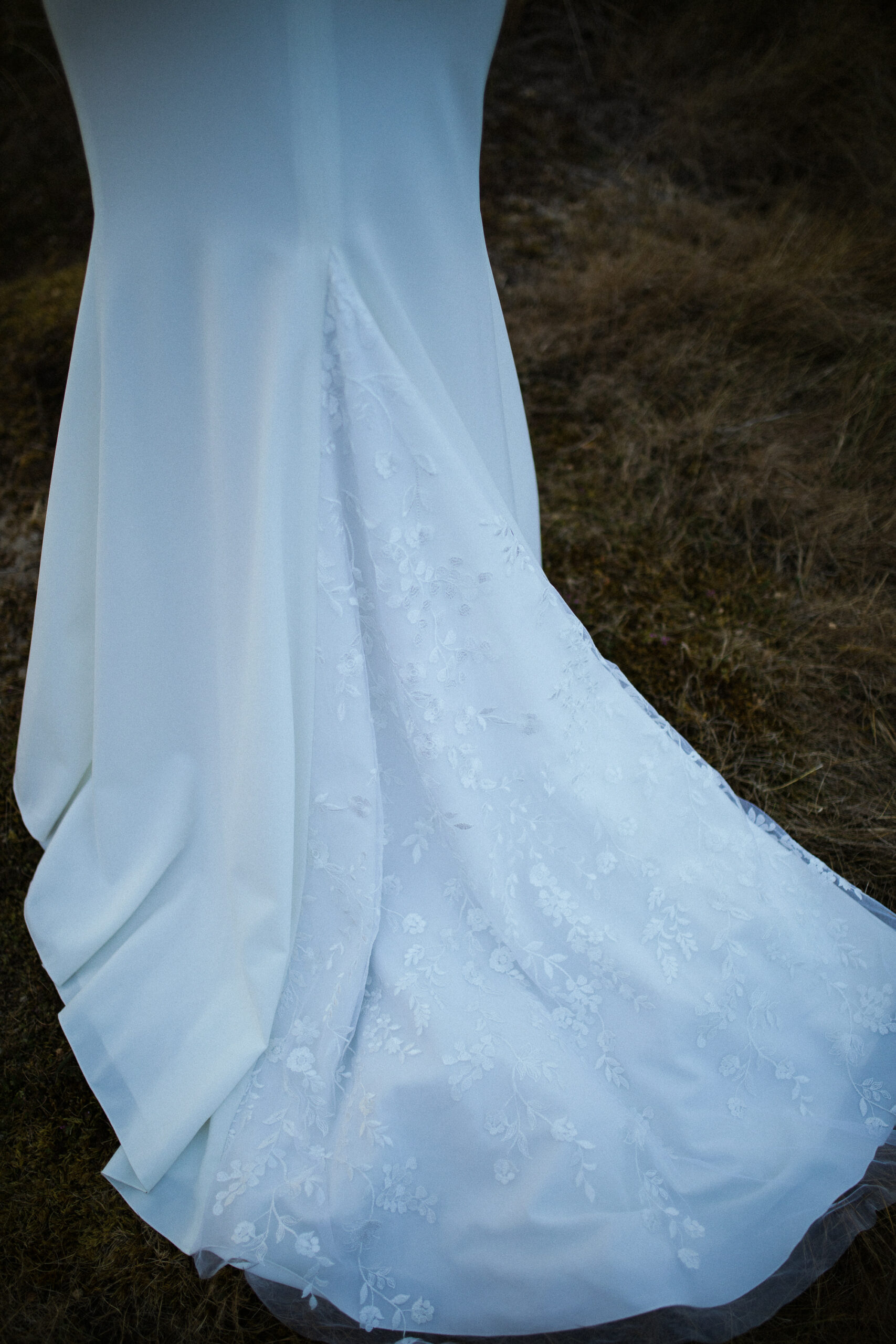 Femme rousse portant une robe de mariée en dentelle dans les dunes végétales en bord de mer.