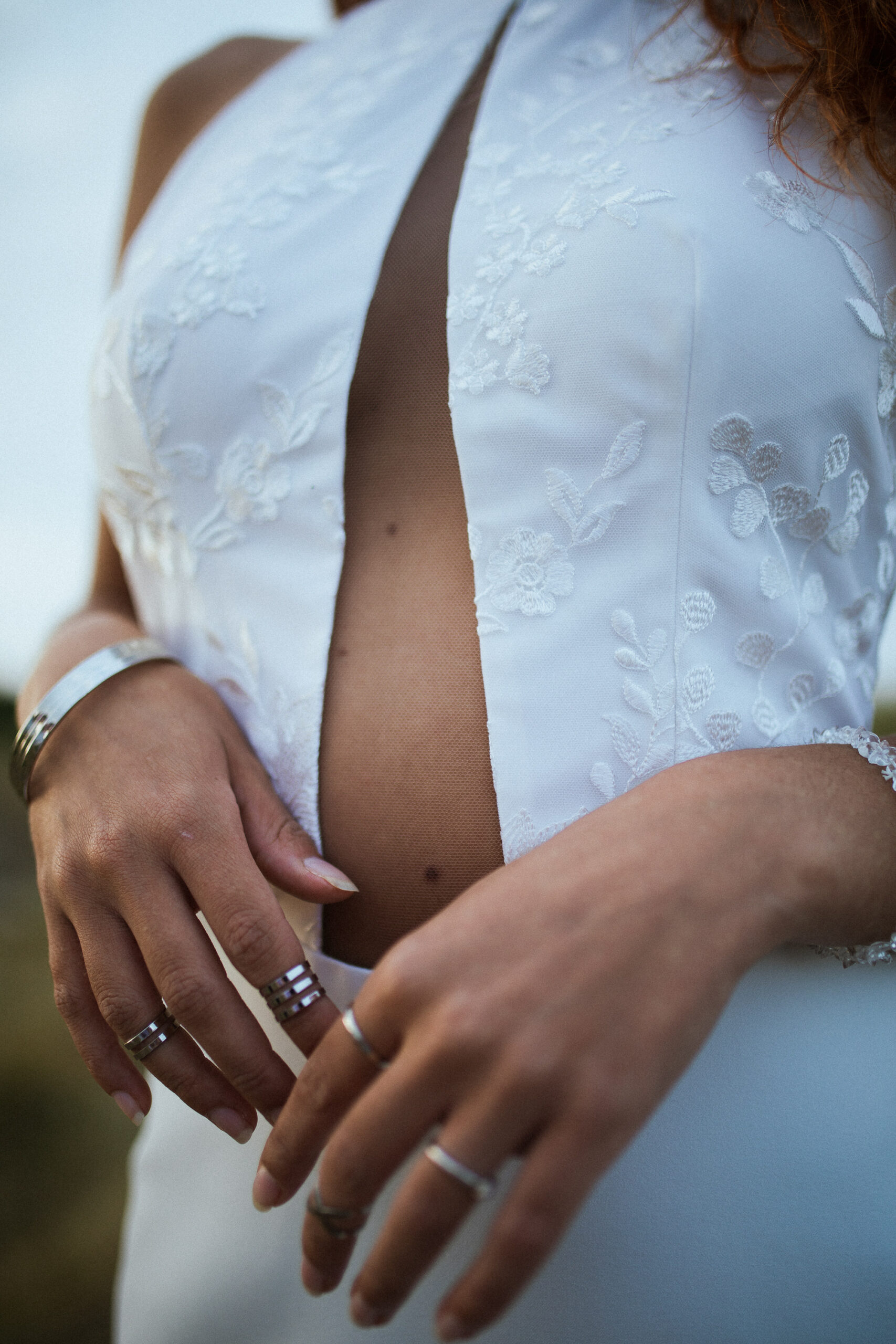 Femme rousse portant une robe de mariée en dentelle dans les dunes végétales en bord de mer.