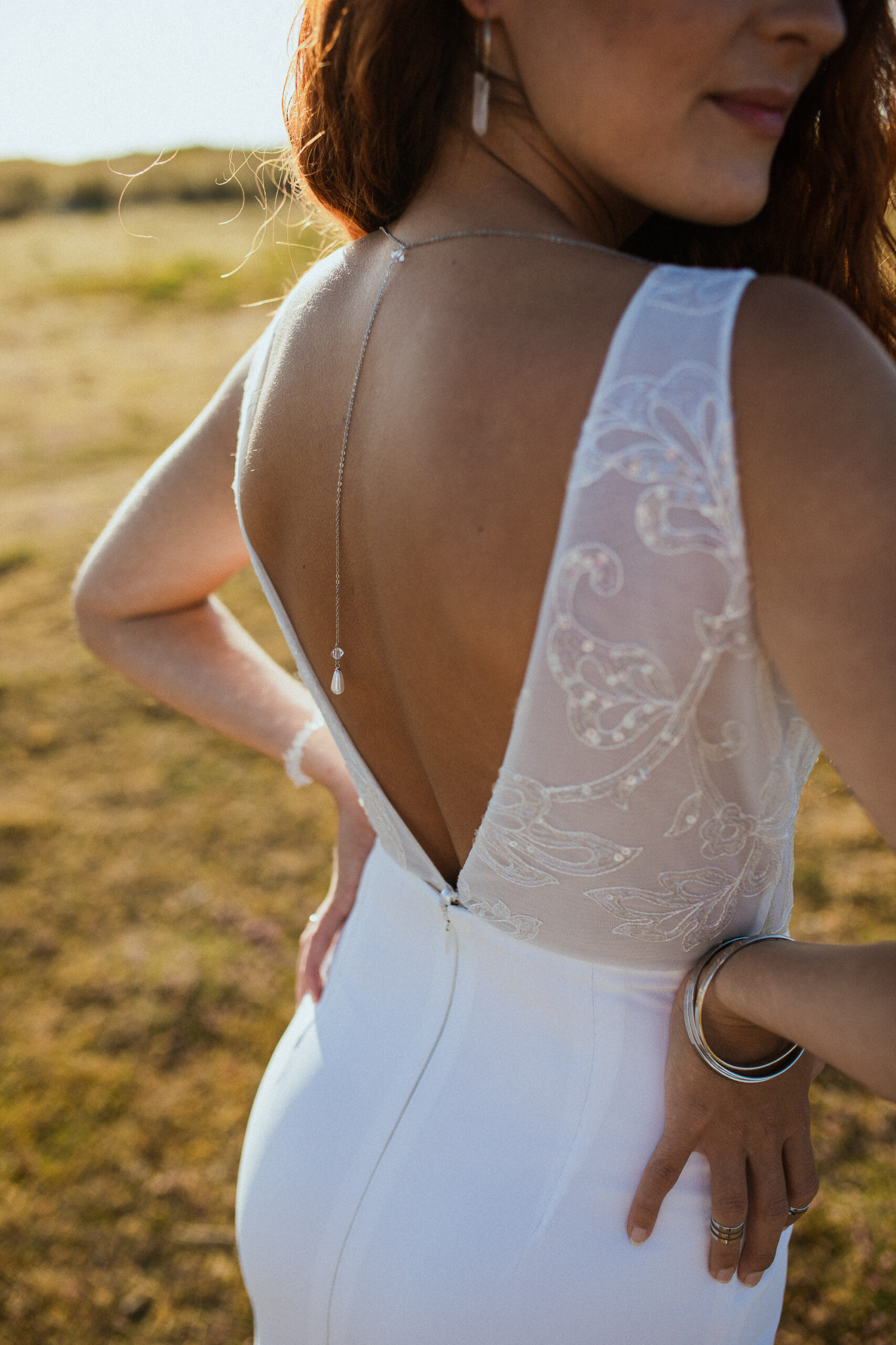 Femme rousse portant une robe de mariée en dentelle dans les dunes végétales en bord de mer.