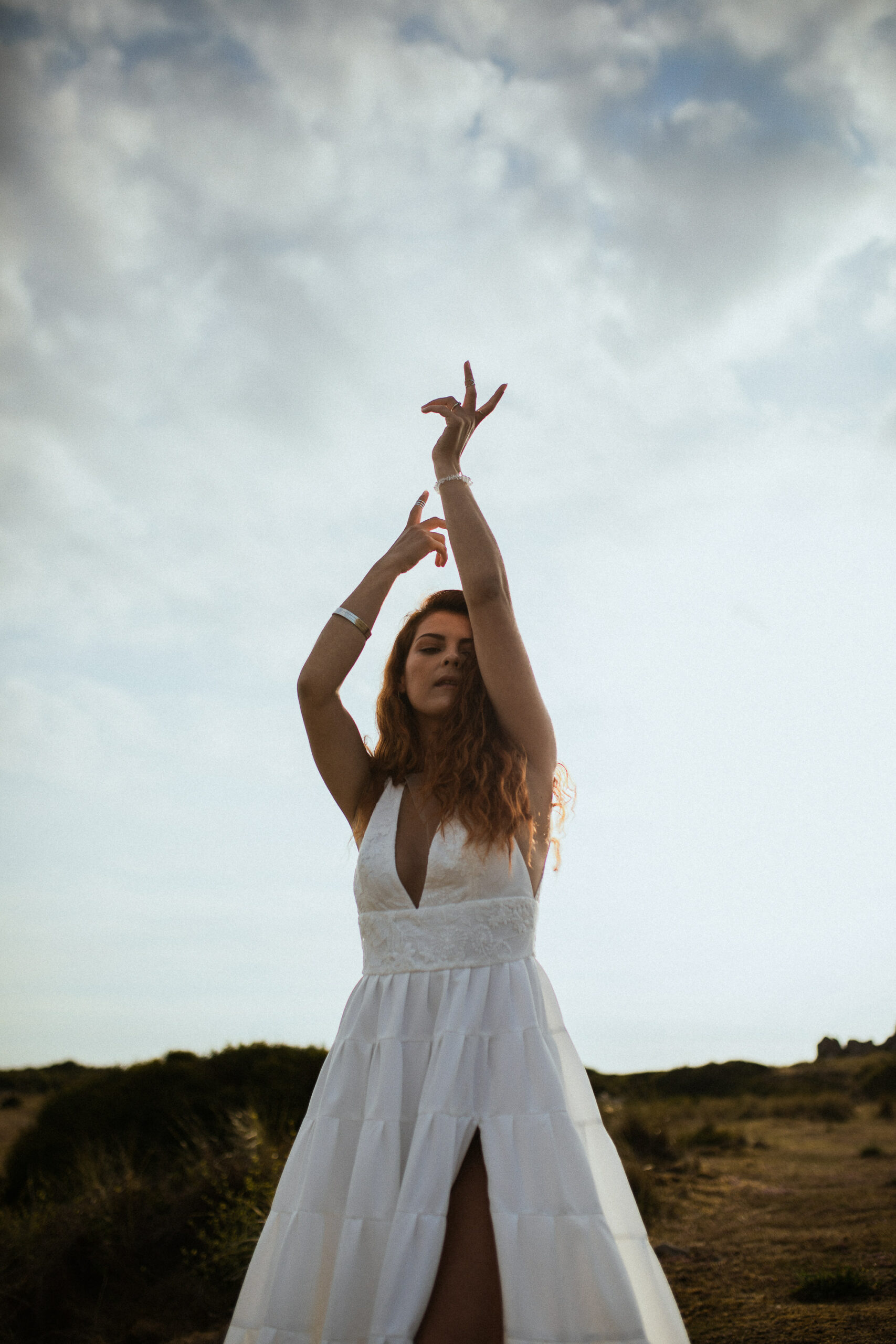 Femme rousse portant une robe de mariée en dentelle dans les dunes végétales en bord de mer.