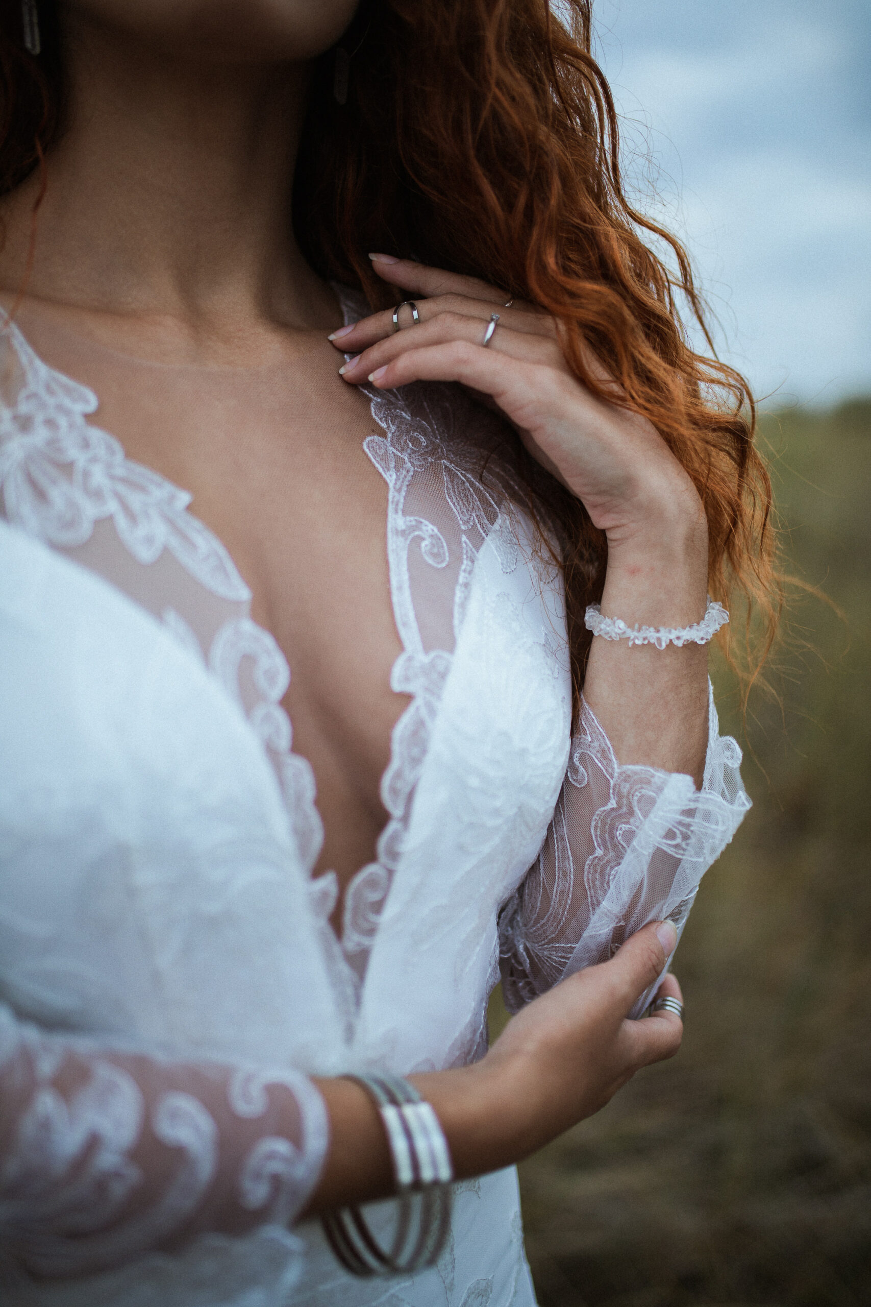 Femme rousse portant une robe de mariée en dentelle dans les dunes végétales en bord de mer.