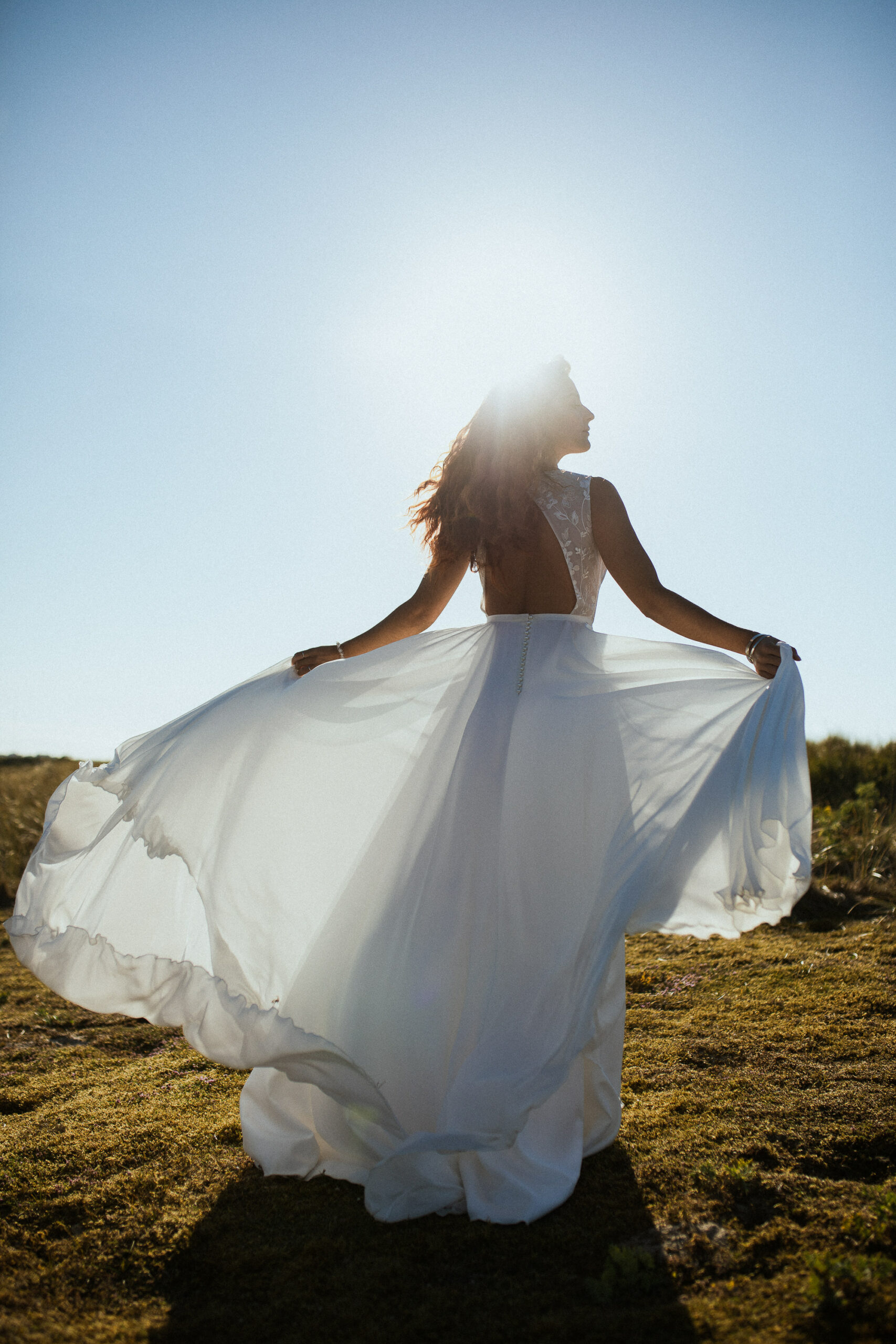 Femme rousse portant une robe de mariée en dentelle dans les dunes végétales en bord de mer.