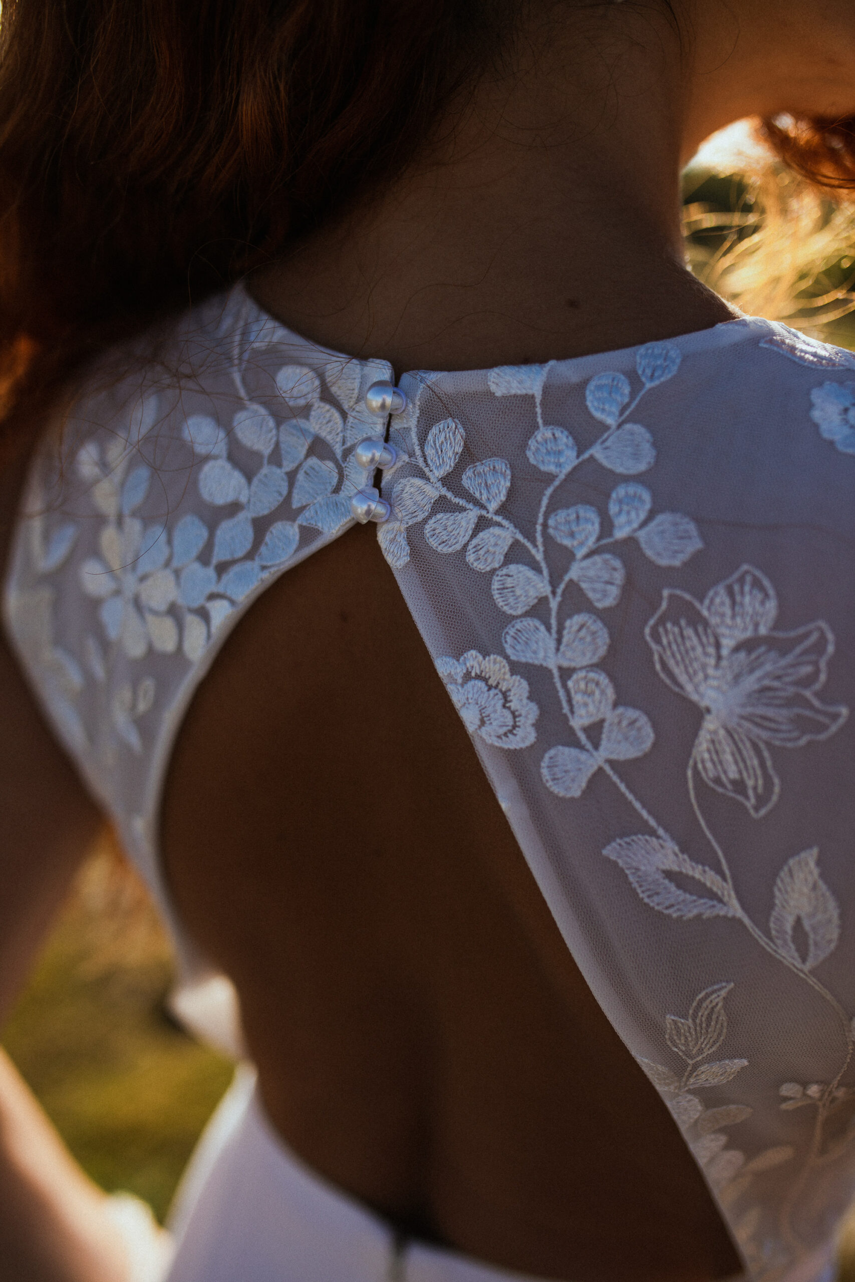 Femme rousse portant une robe de mariée en dentelle dans les dunes végétales en bord de mer.