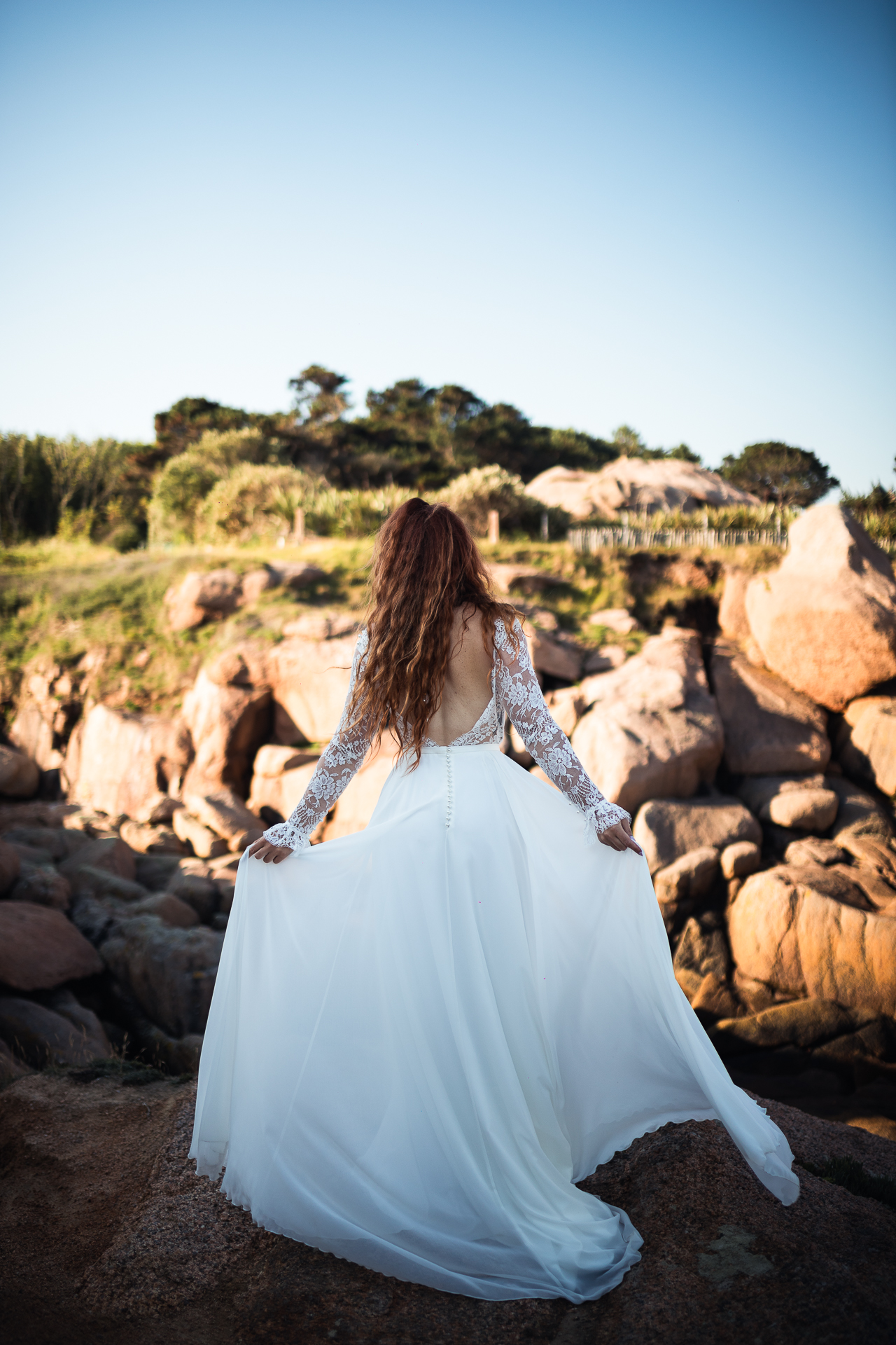 Femme portant une robe de mariée bohème en dentelle au bord de la mer en Bretagne.