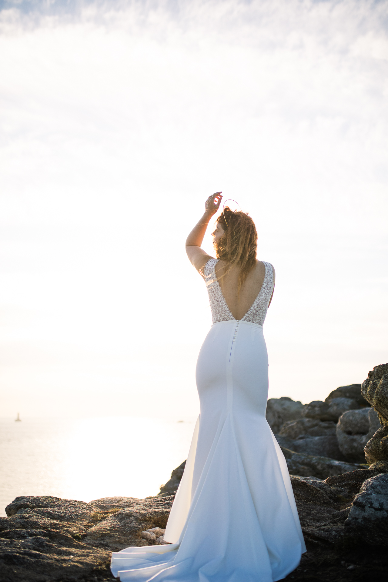 Femme portant une robe de mariée en dentelle au bord de la mer en Bretagne.