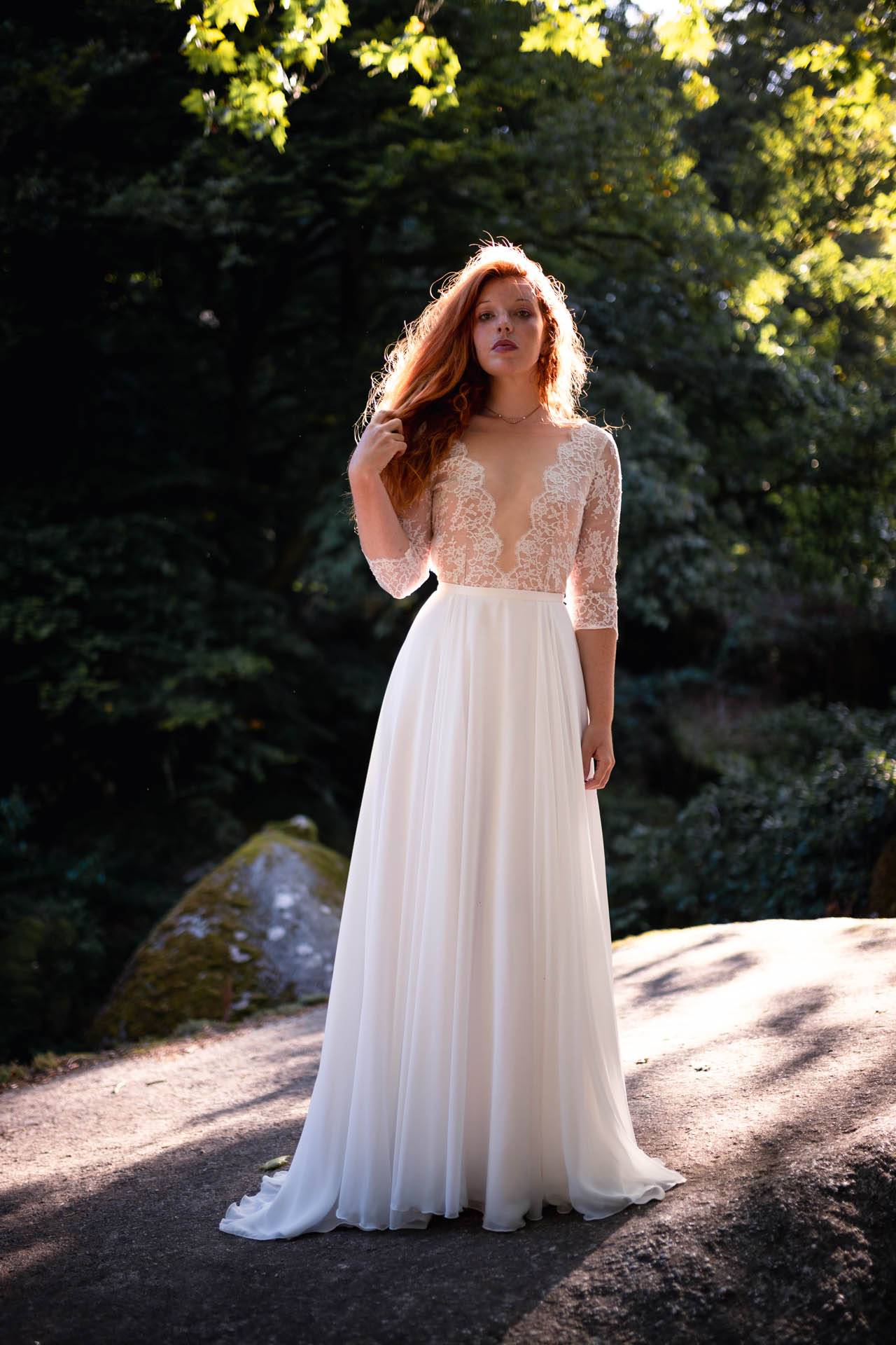 Femme portant une robe de mariée avec décolleté et manches en dentelle dans la nature.