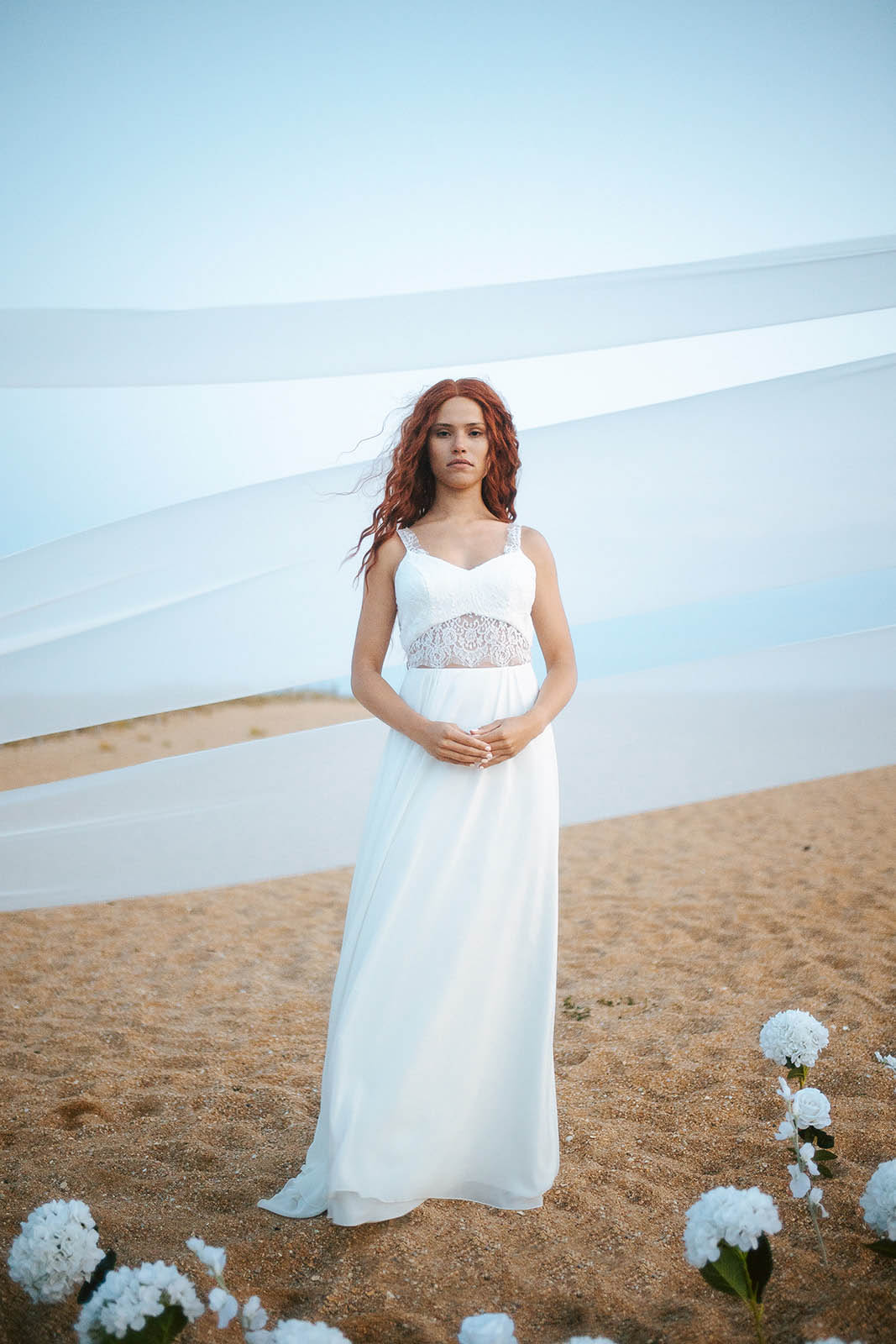 Femme rousse portant une robe de mariée de créateur en dentelle sur-mesure à la plage.