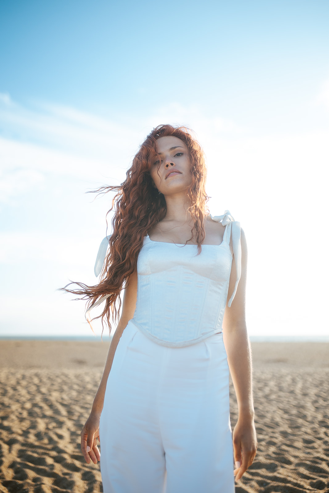 Femme rousse portant une robe de mariée de créateur en dentelle sur-mesure à la plage.