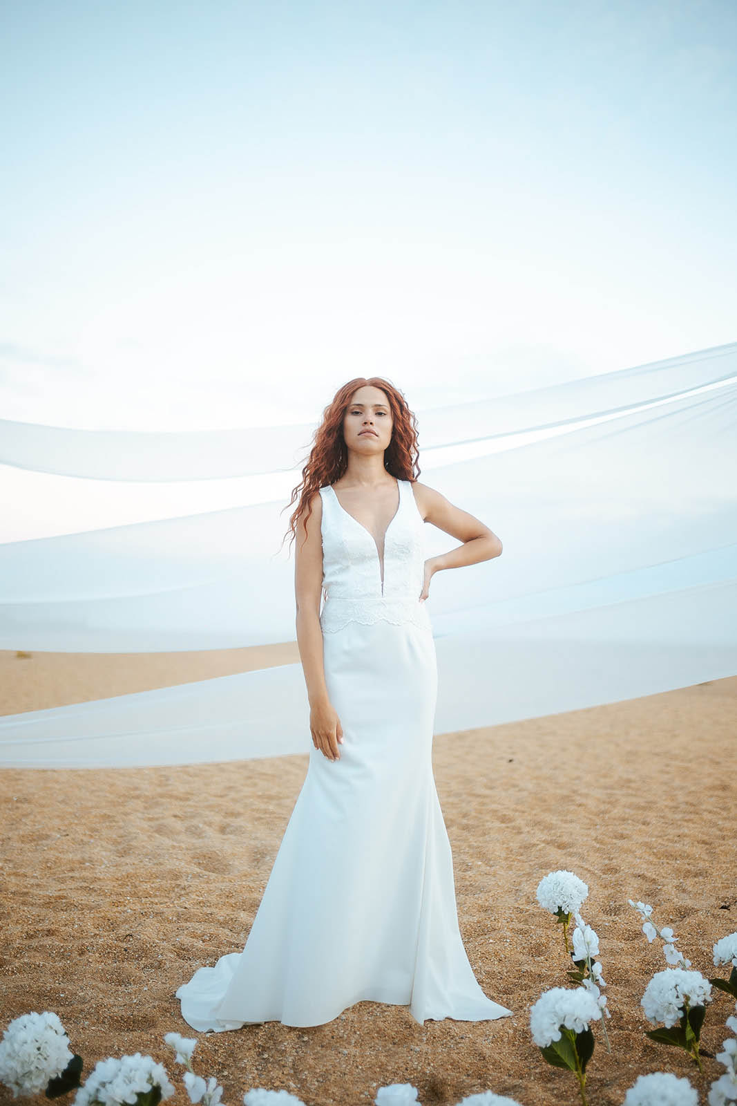 Femme rousse portant une robe de mariée de créateur en dentelle sur-mesure à la plage.