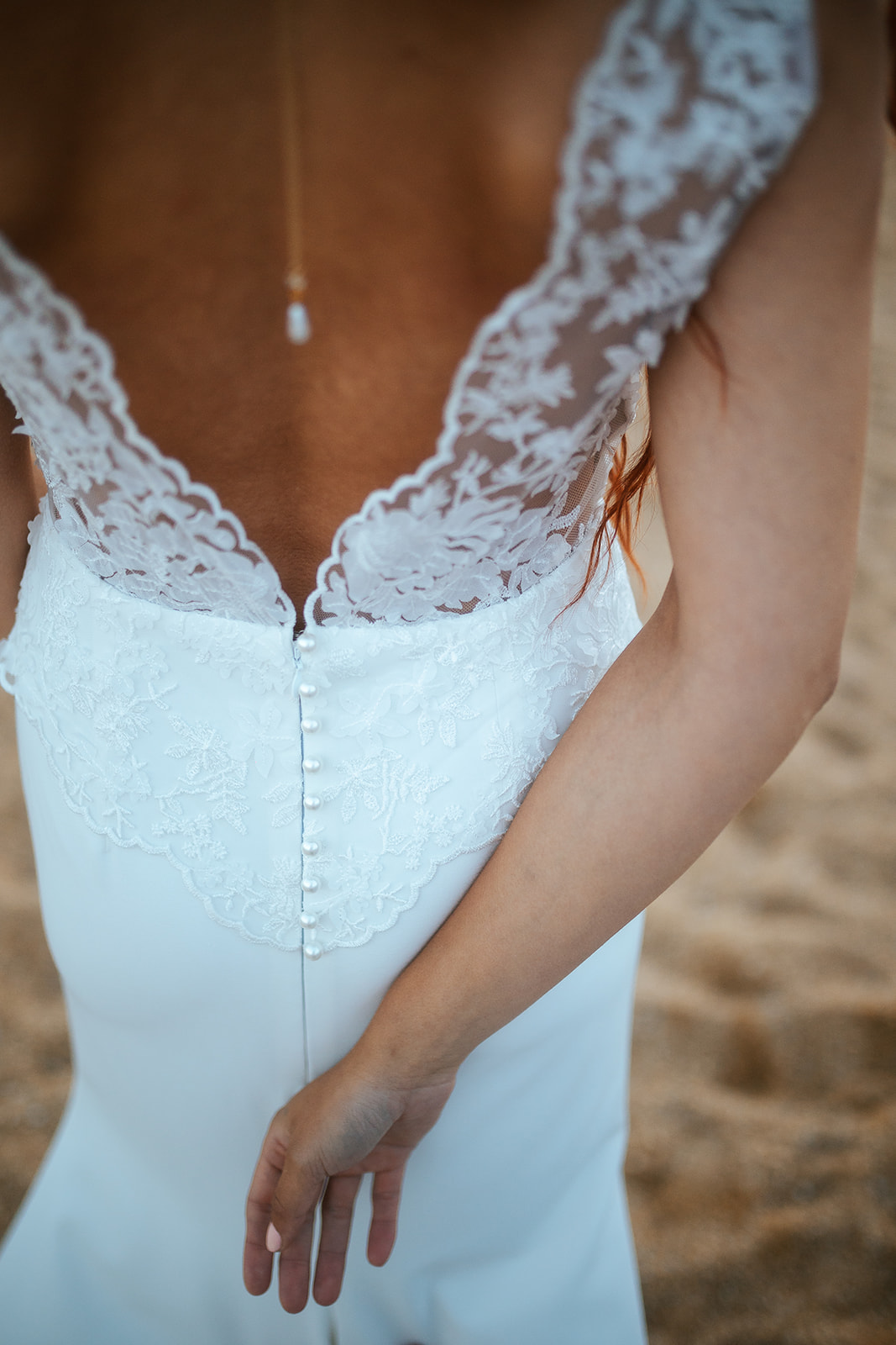 Femme rousse portant une robe de mariée de créateur en dentelle sur-mesure à la plage.