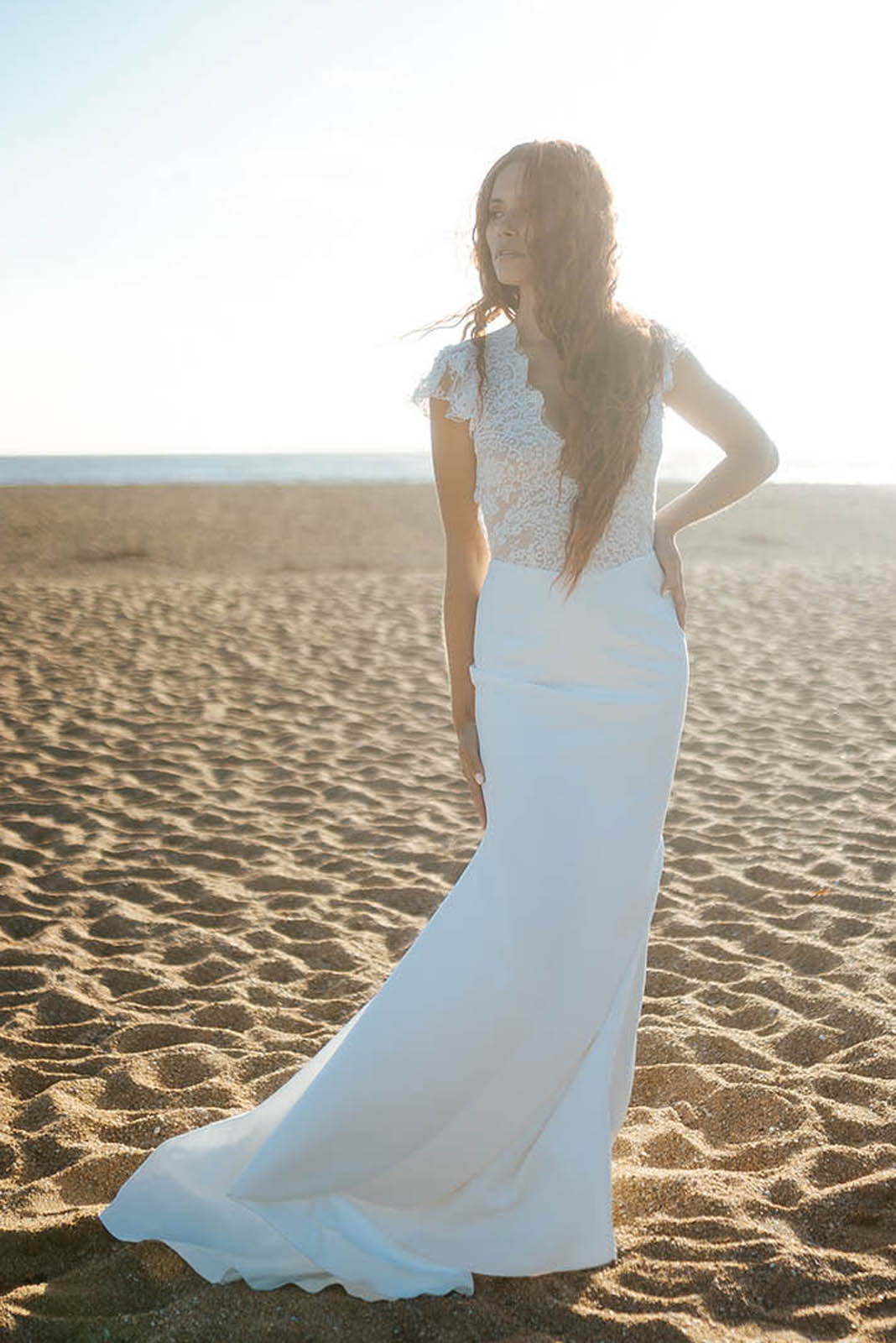 Femme rousse portant une robe de mariée de créateur en dentelle sur-mesure à la plage.