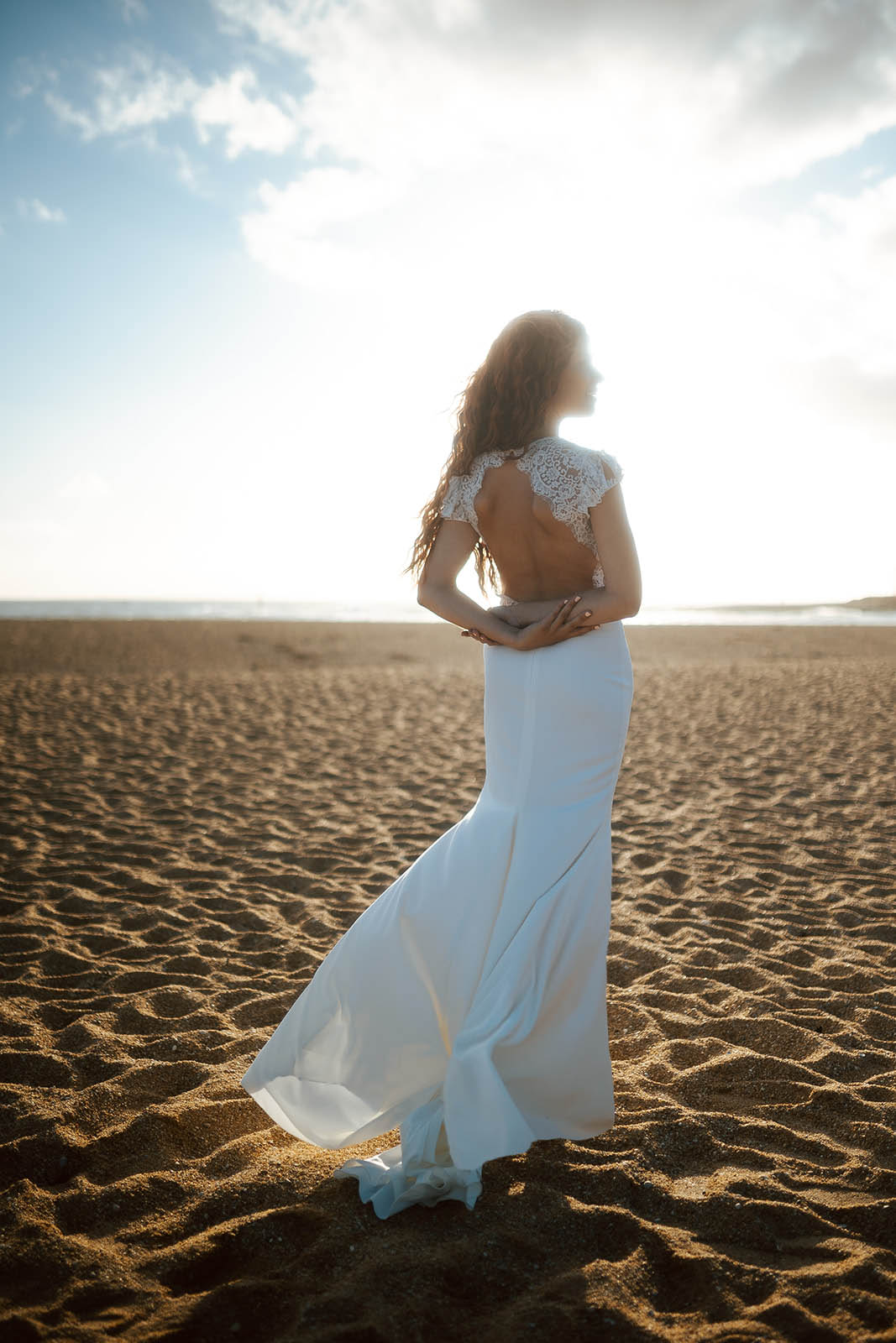 Femme rousse portant une robe de mariée de créateur en dentelle sur-mesure à la plage.