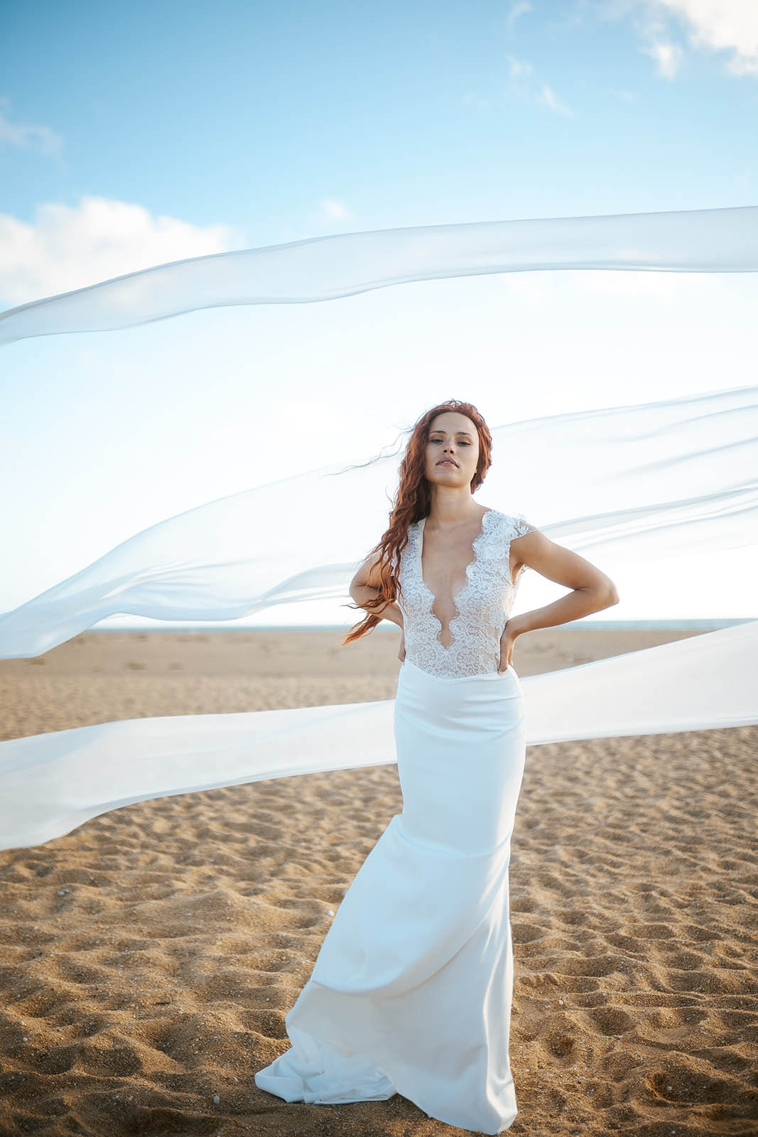 Femme rousse portant une robe de mariée de créateur en dentelle sur-mesure à la plage.