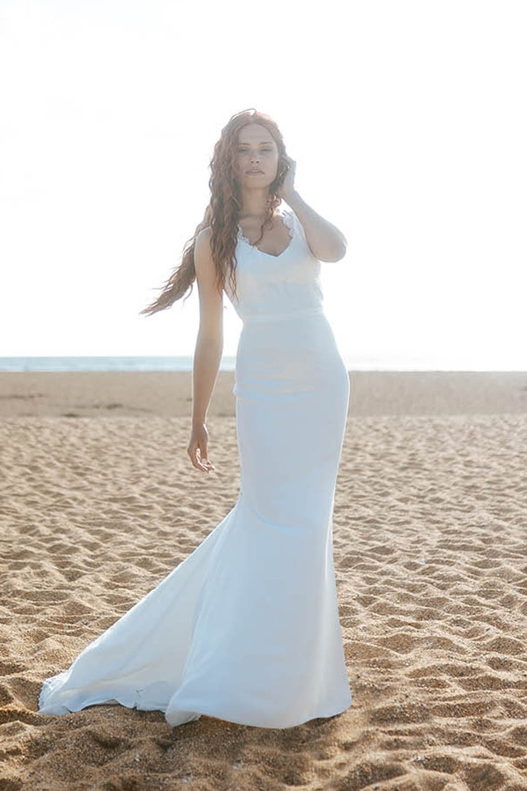 Femme rousse portant une robe de mariée de créateur en dentelle sur-mesure à la plage.