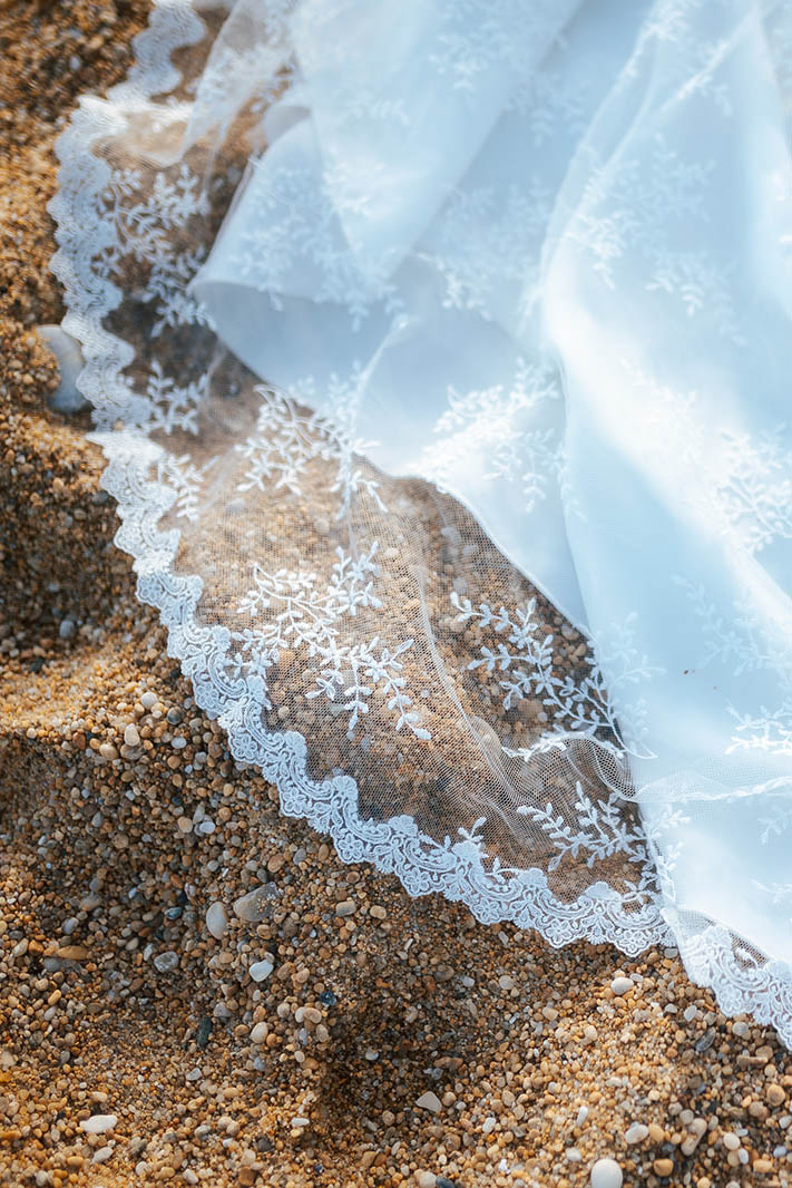 Femme rousse portant une robe de mariée de créateur en dentelle sur-mesure à la plage.