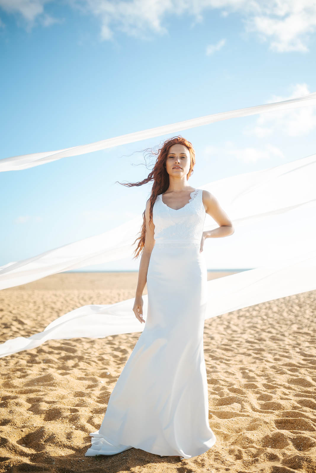 Femme rousse portant une robe de mariée de créateur en dentelle sur-mesure à la plage.