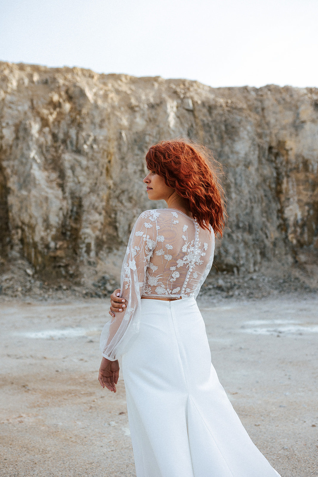 Femme rousse portant une robe de mariée bohème de créateur en dentelle sur-mesure.