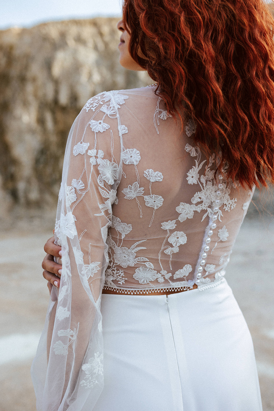 Femme rousse portant une robe de mariée bohème de créateur en dentelle sur-mesure.