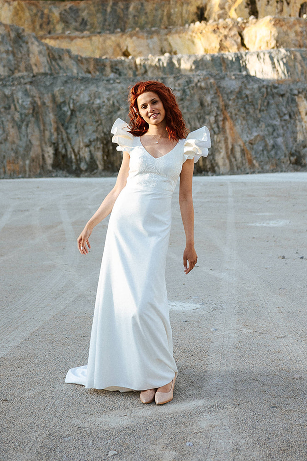 Femme rousse portant une robe de mariée à épaulettes de créateur en dentelle sur-mesure.